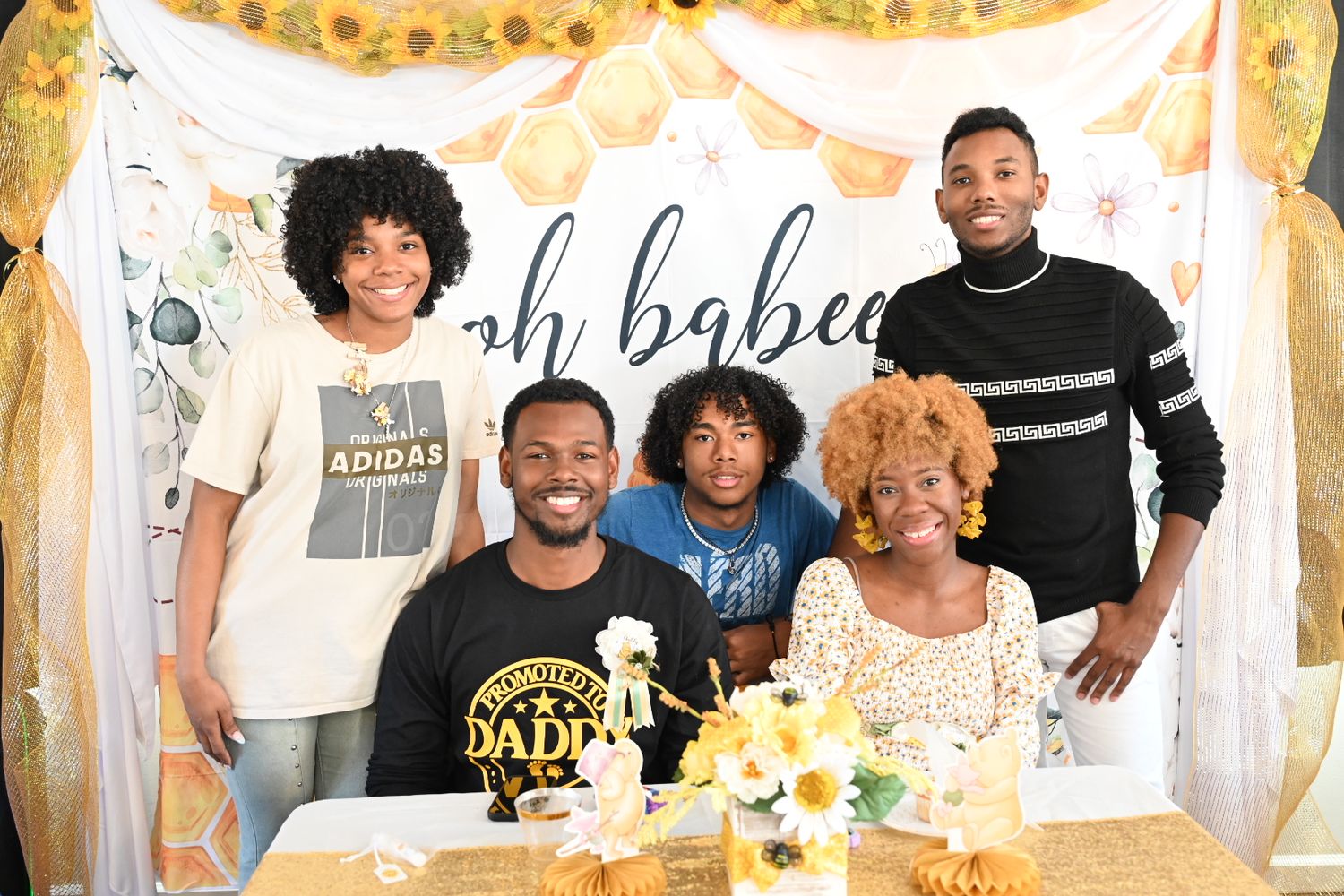 Family of five posing together at a bee-themed baby shower with yellow floral table decorations.
