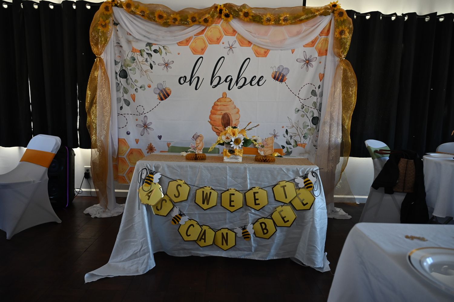 Full view of Oh Babee baby shower setup with yellow tulle arch, floral backdrop, and honeycomb banner.