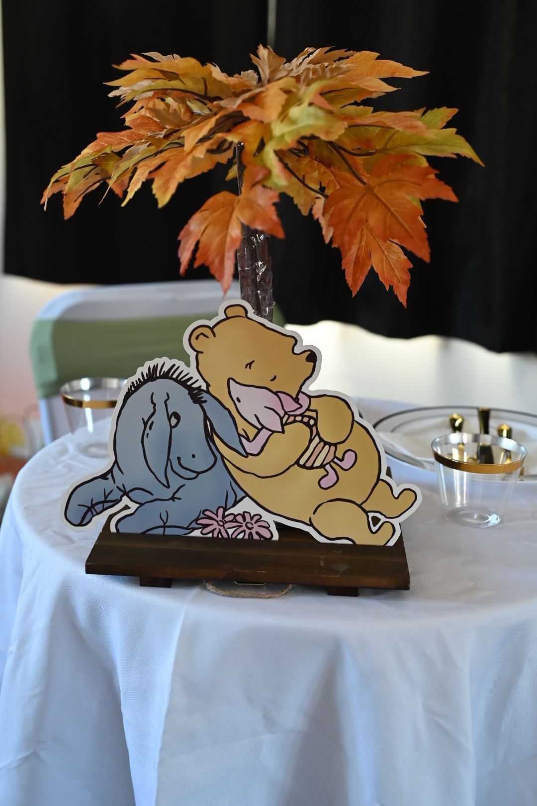 Winnie the Pooh and Eeyore centerpiece with autumn maple leaves in a vase on a white tablecloth.