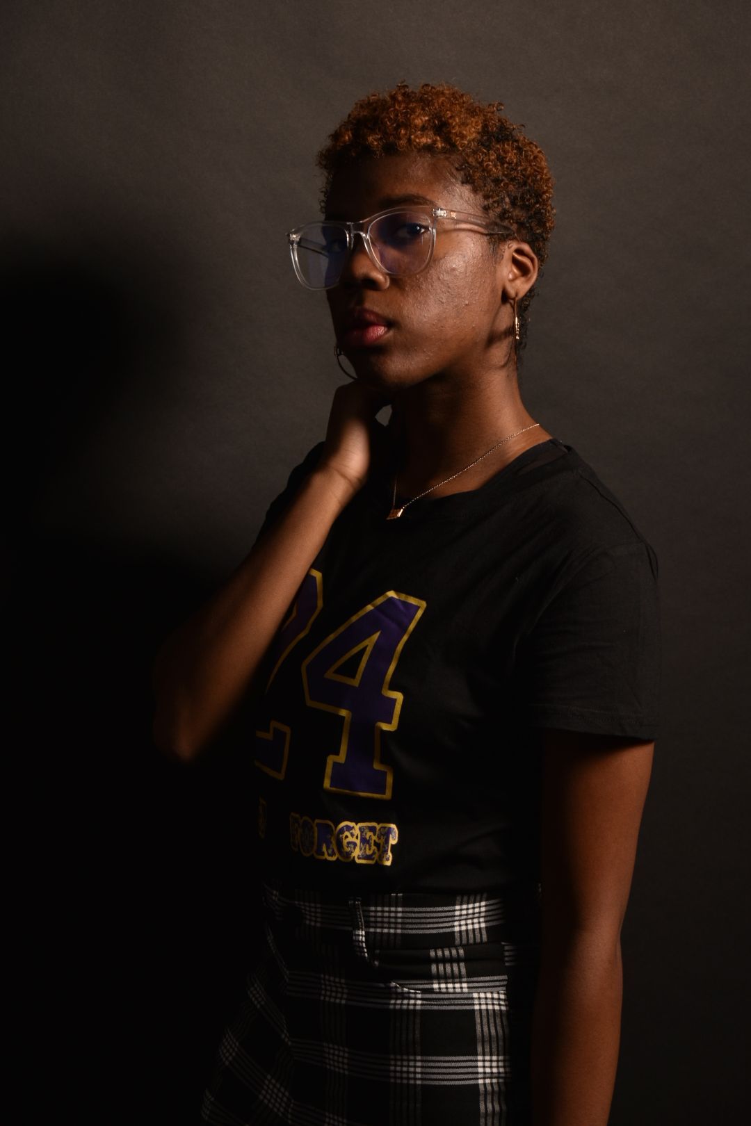 Stylish young woman in black number 24 jersey and clear glasses poses in dramatic studio lighting.