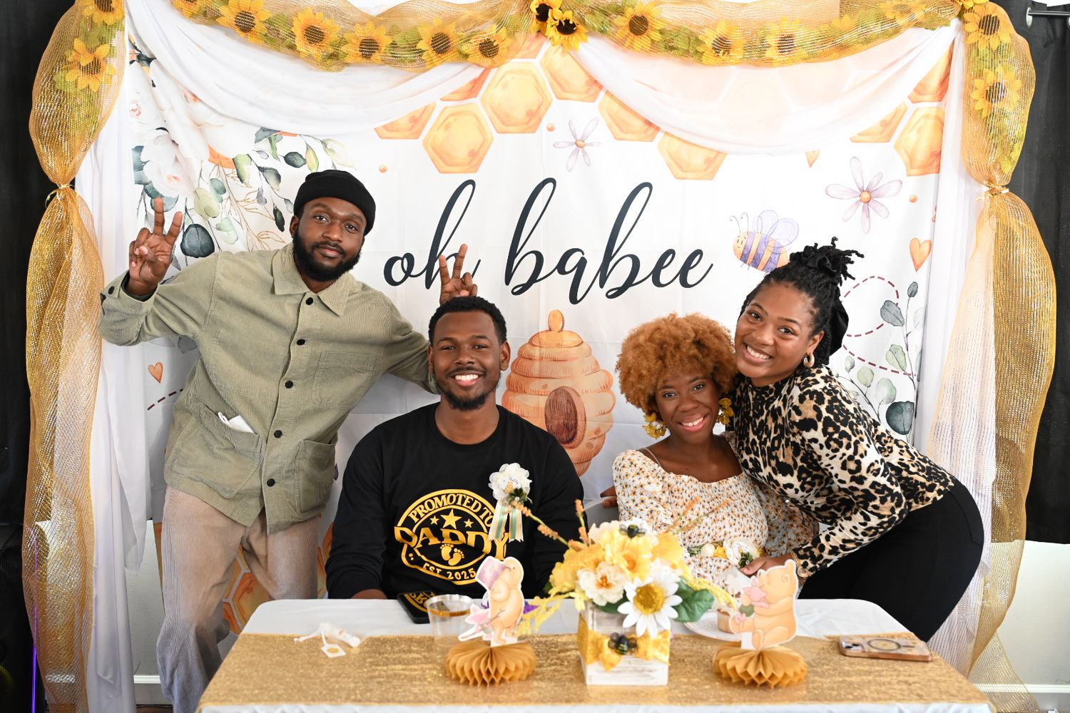 Four people posing and smiling at a bee-themed oh babee baby shower with sunflower decor.