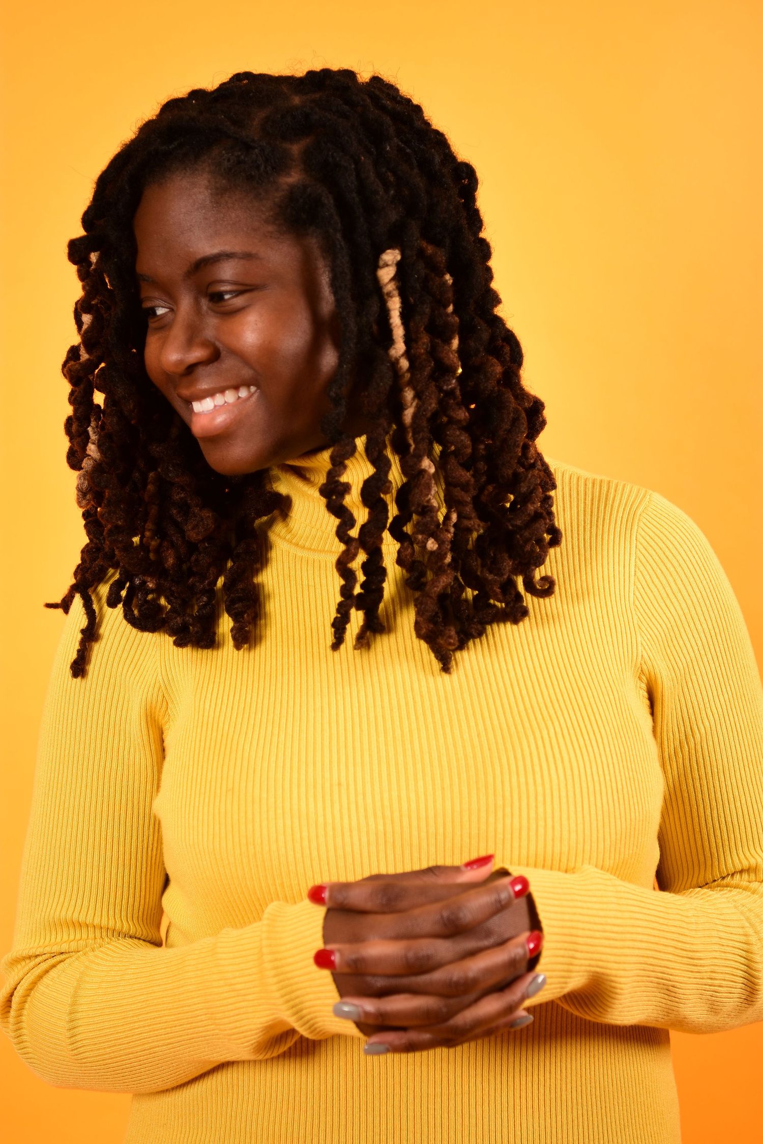 Smiling woman with locs wearing yellow turtleneck against bright yellow background.