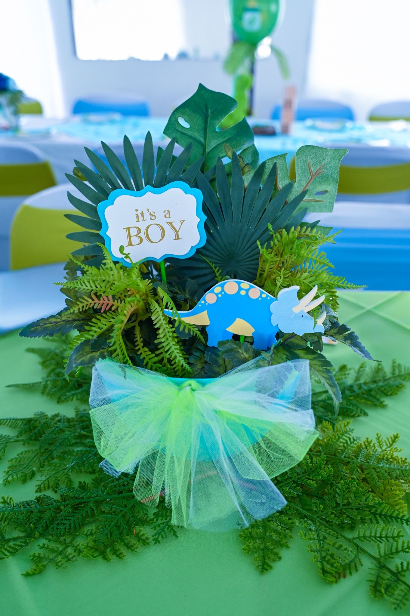 It's a Boy dinosaur centerpiece with tropical leaves, blue triceratops, and green tulle.