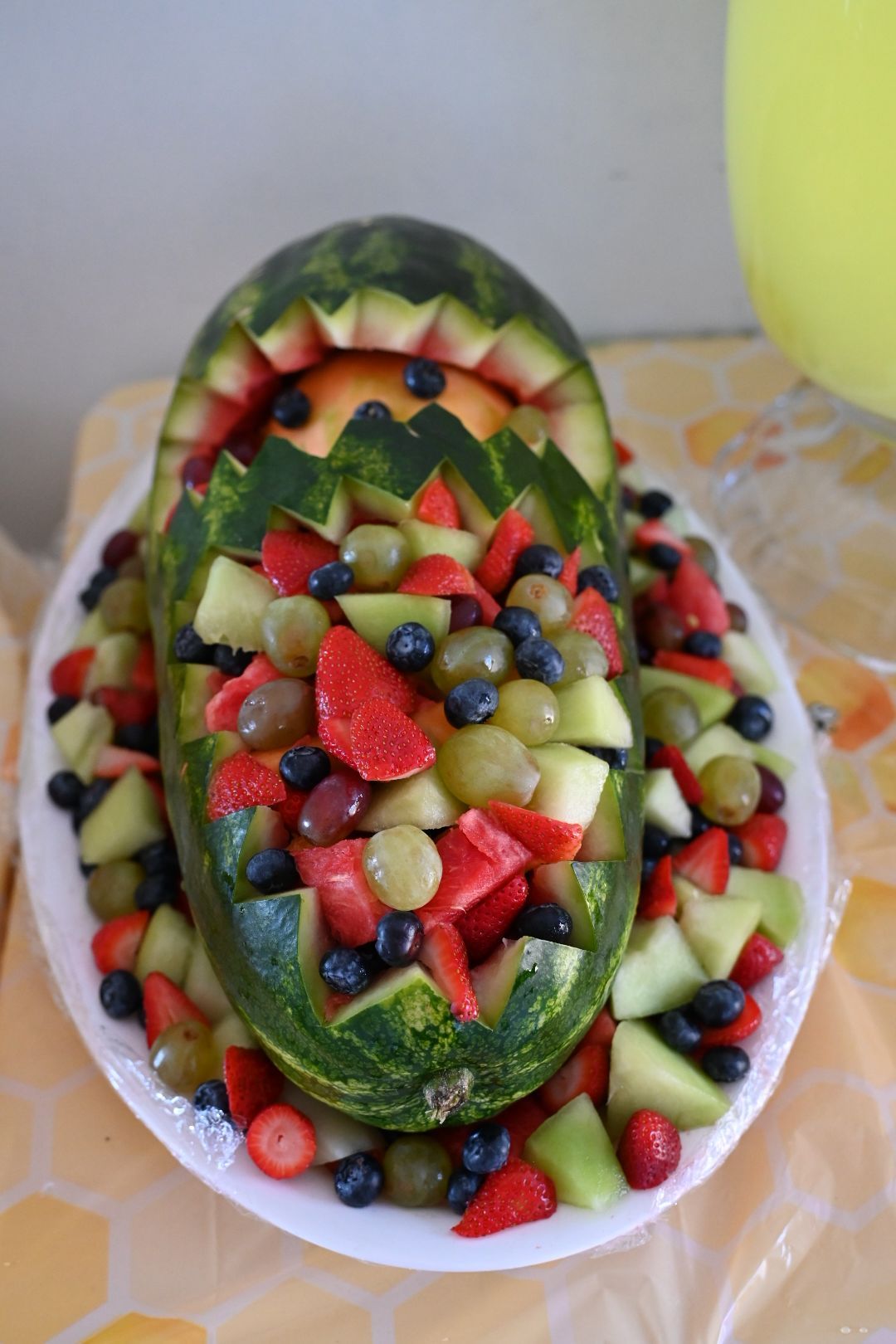 Carved watermelon baby carriage filled with fresh fruit salad including strawberries, blueberries, and grapes.