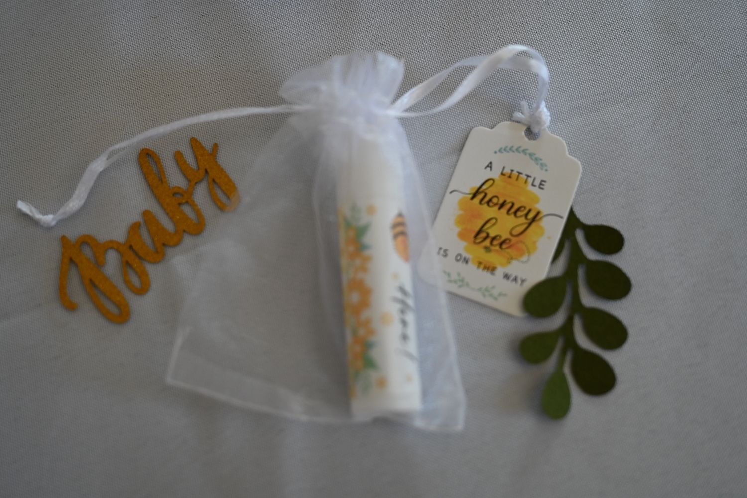 Honey bee baby shower favor with lip balm in white organza bag tagged a little honey bee is on the way.