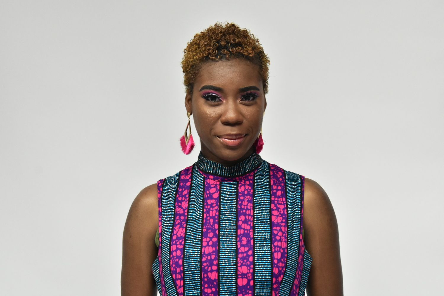 Close-up portrait of woman in colorful African print turtleneck dress with pink drop earrings.