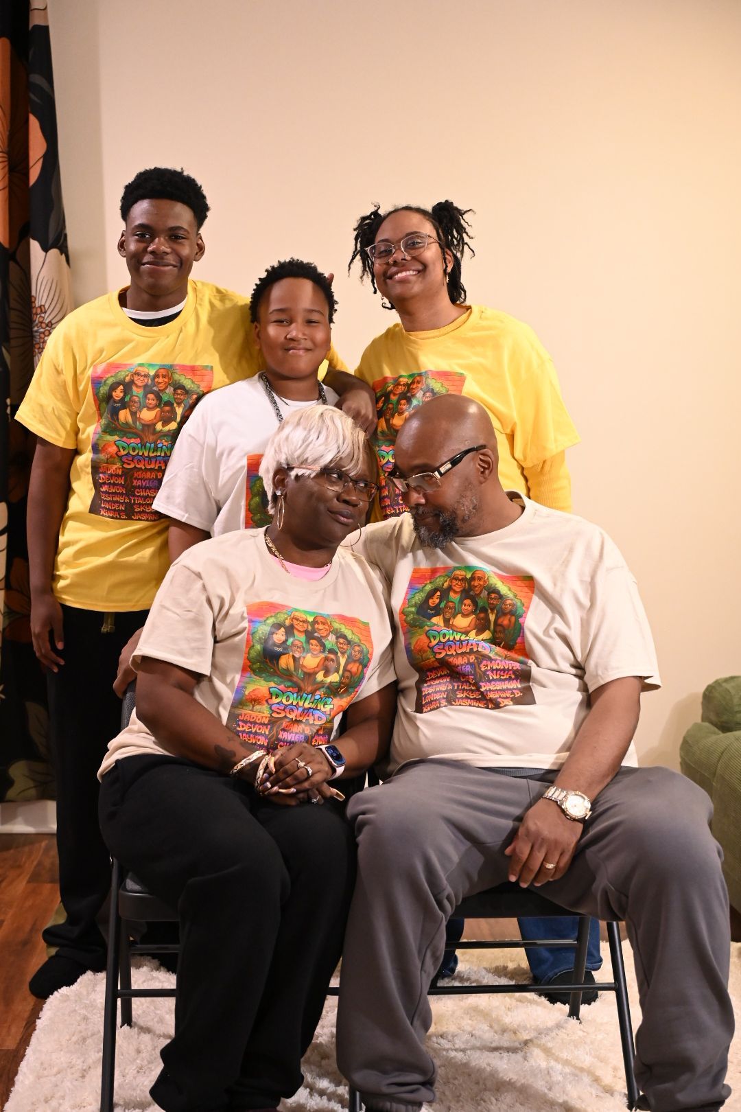 Family of five posing together in matching graphic t-shirts, with two seated adults and three standing children behind them.