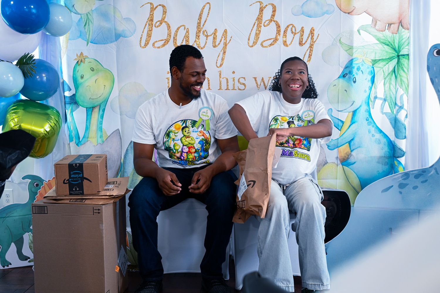 Smiling couple opening presents at a colorful Baby Boy baby shower with balloon decorations.