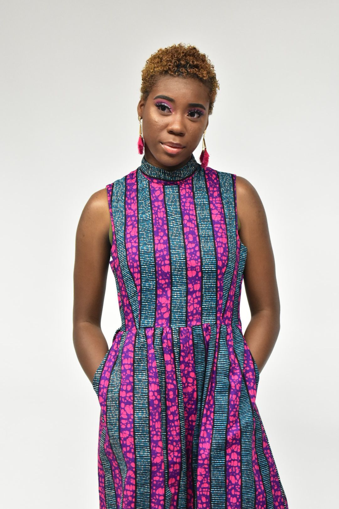 Woman in bold African print midi dress with hands in pockets posing on white background.