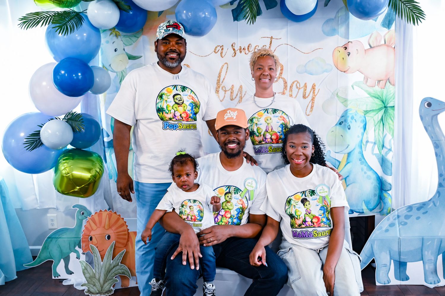 Family of five smiling at a dinosaur baby boy party with blue and green balloons.