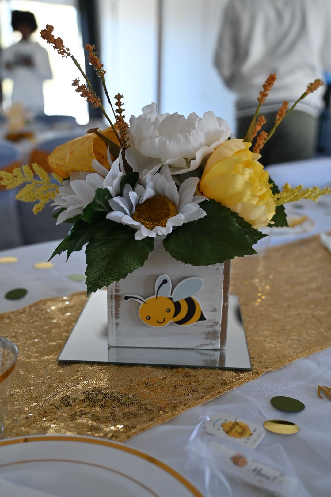 Bumble bee baby shower centerpiece featuring white and yellow flowers in decorated wooden box on mirror.