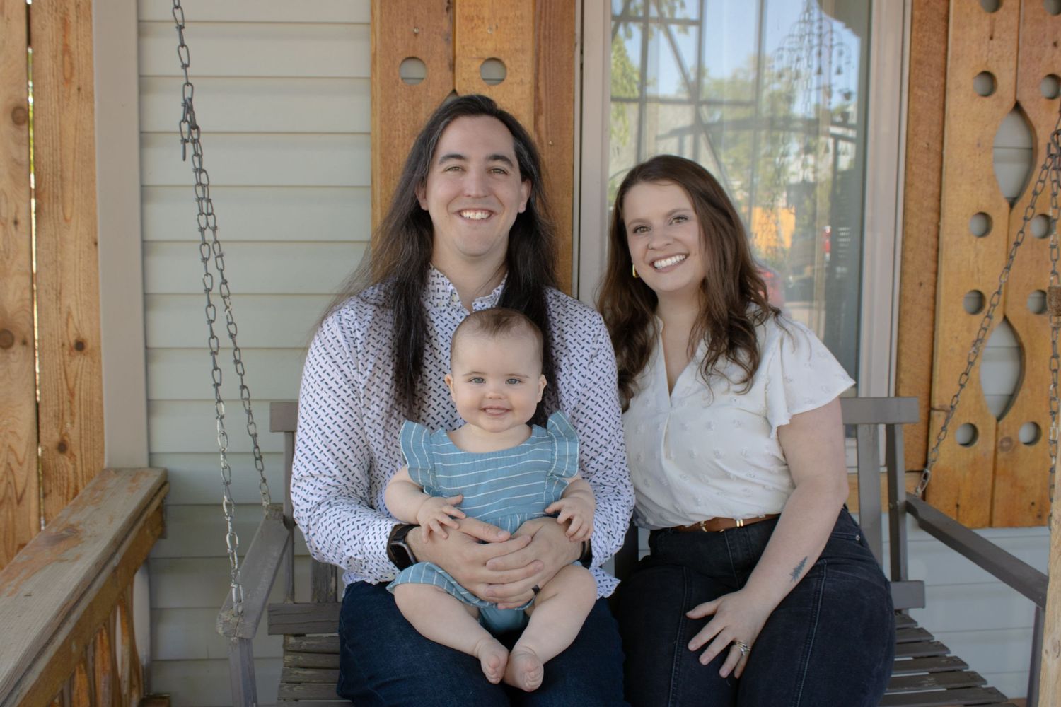 Family portrait with a baby sitting together smiling on a porch swing.