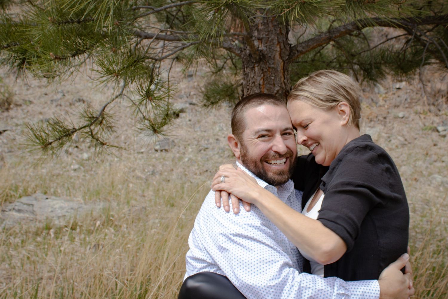 Happy couple embracing and laughing together outdoors in a dry grassy mountain landscape.