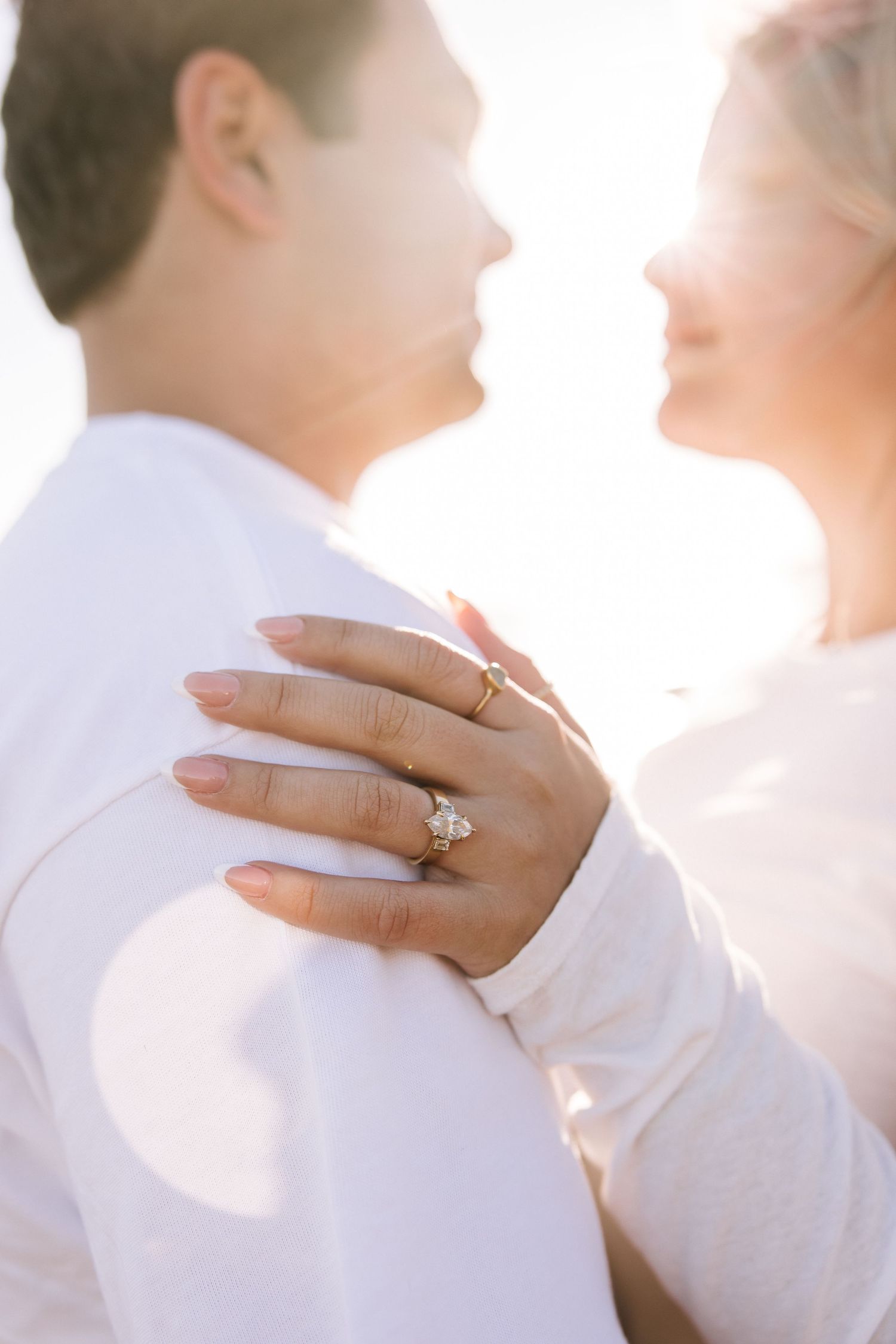 Close-up of engagement ring on womans hand as couple embraces in golden sunlight.