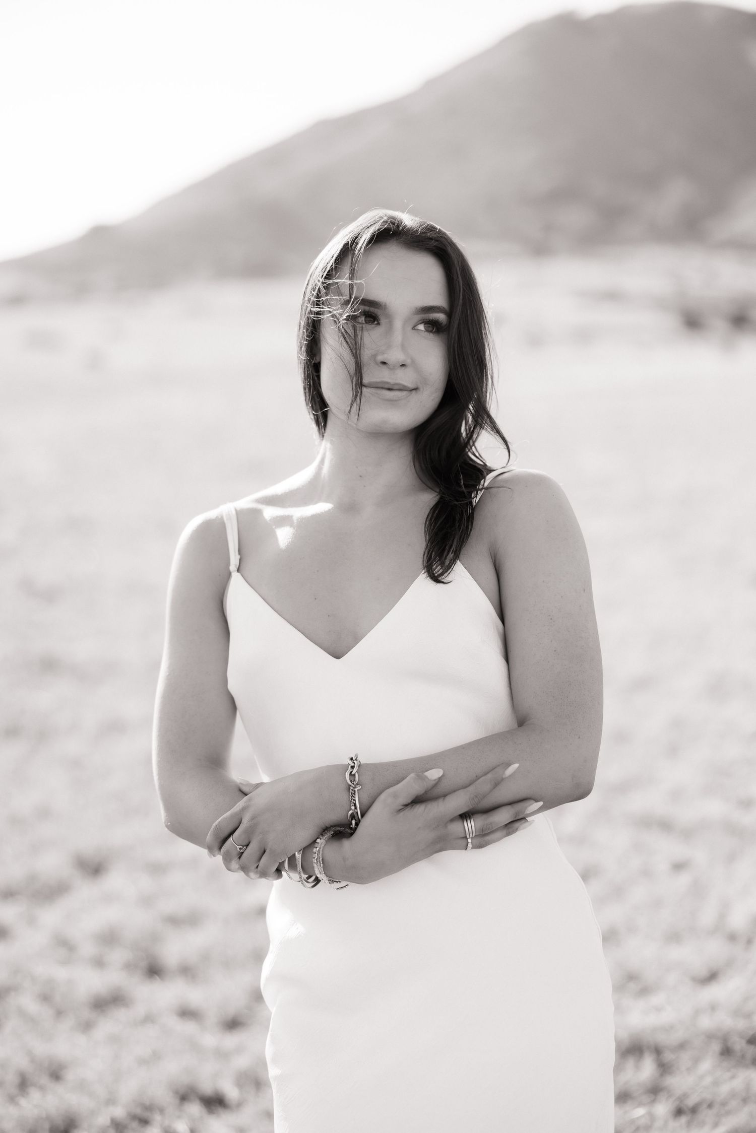 Black and white portrait of brunette woman in white slip dress standing in open field outdoors.