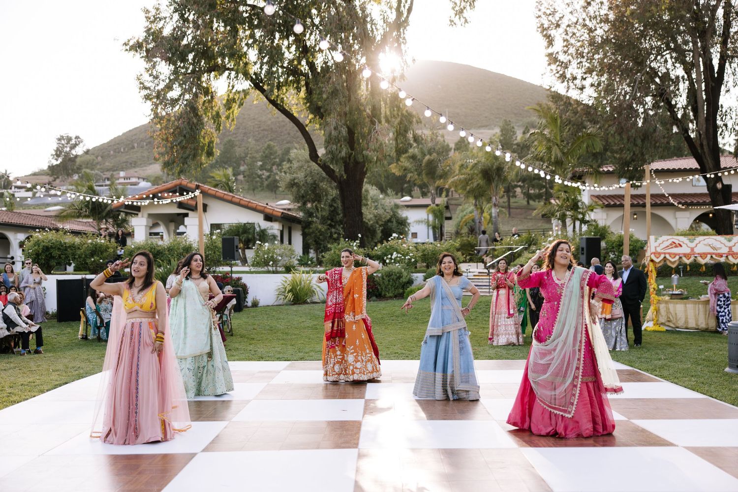 Colorful Indian wedding sangeet dance performance with bridesmaids in vibrant lehengas on outdoor dance floor.