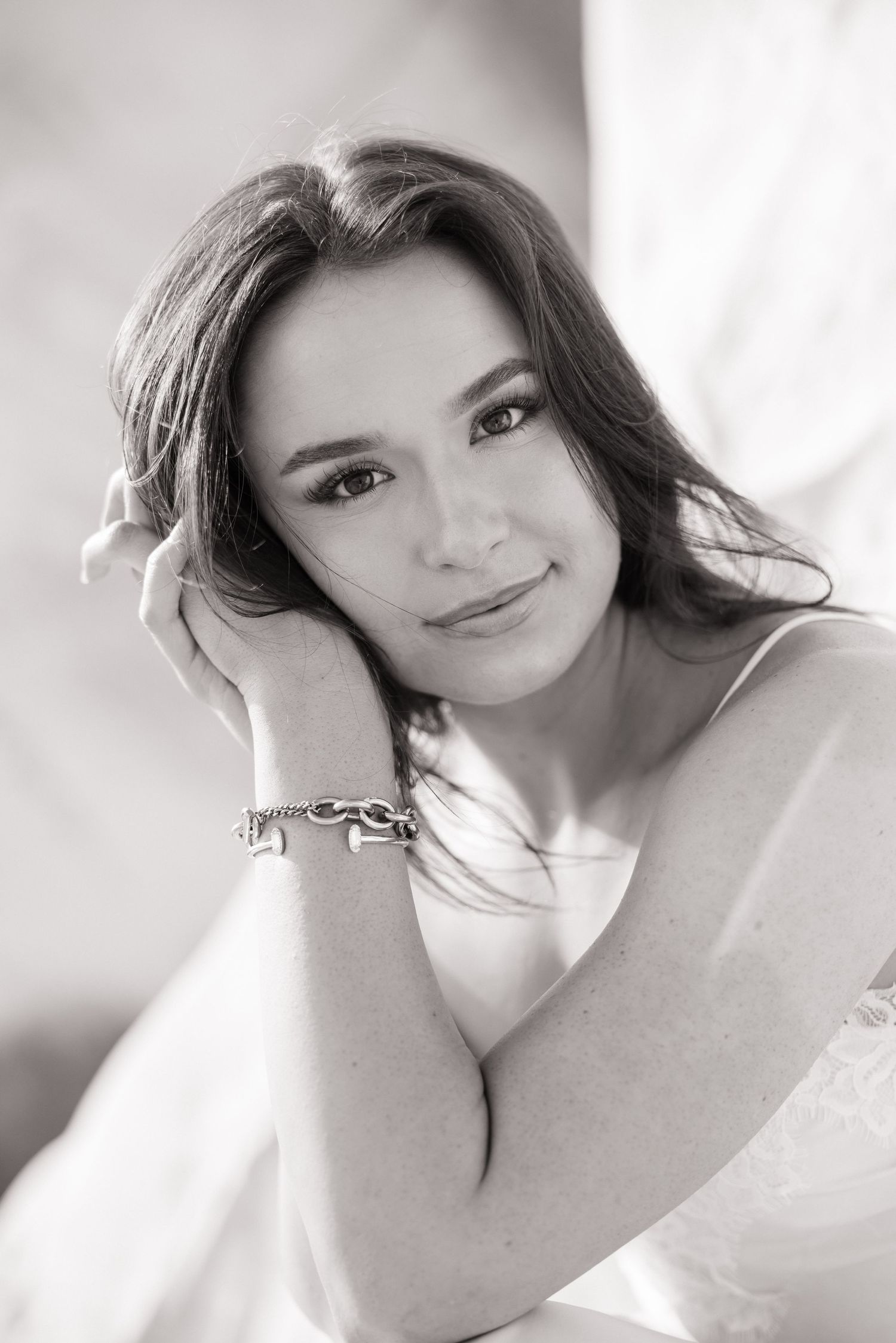 Black and white close-up portrait of brunette woman resting head on hand wearing silver bracelet.