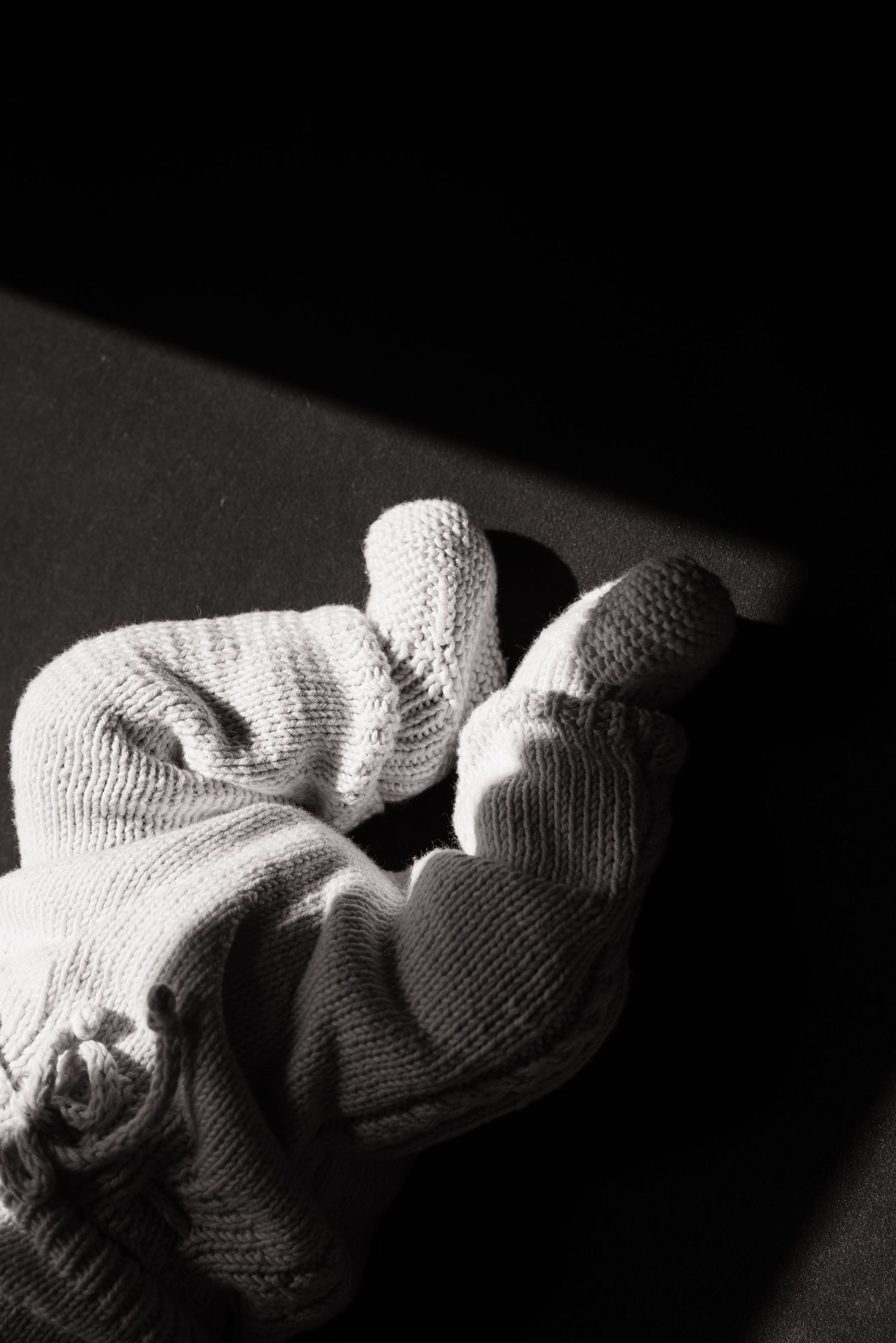 White knitted baby booties photographed in dramatic black and white lighting on dark background.