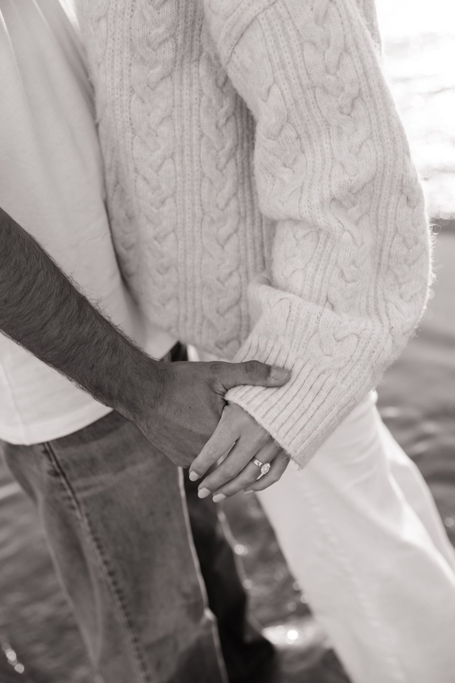Close-up of couple holding hands showing engagement ring in black and white photo.