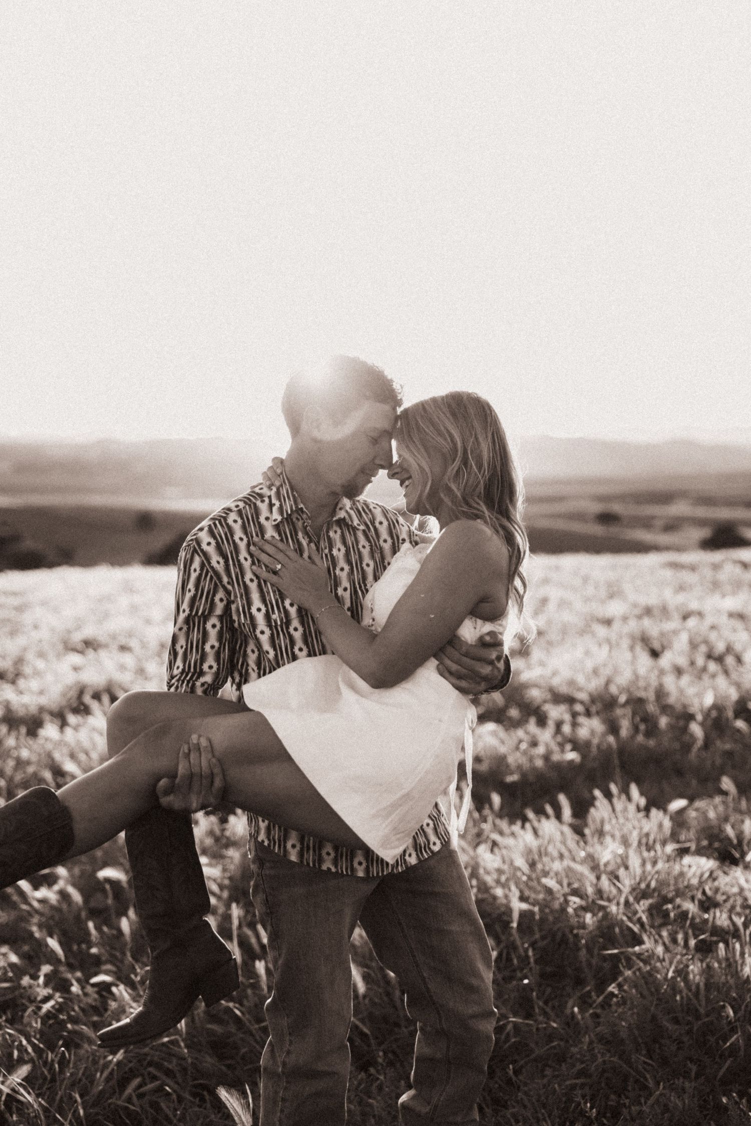 Black and white romantic photo of couple about to kiss in a sunlit field.