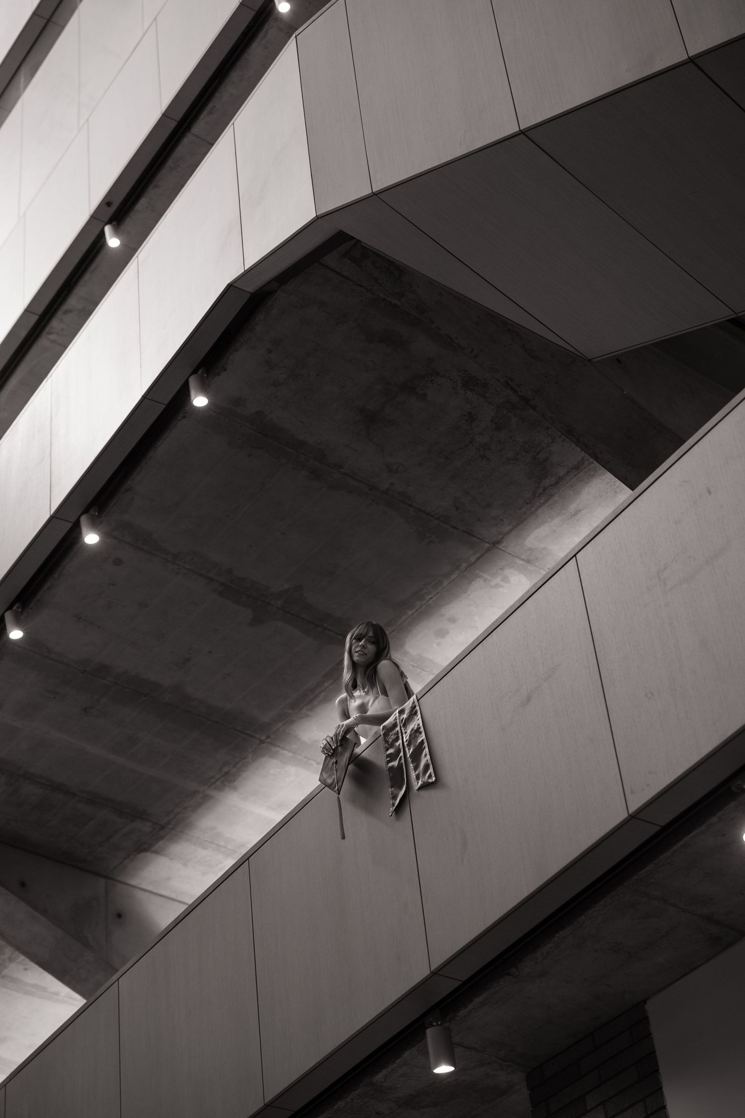 Black and white low angle view of young woman leaning on balcony railing inside modern building.