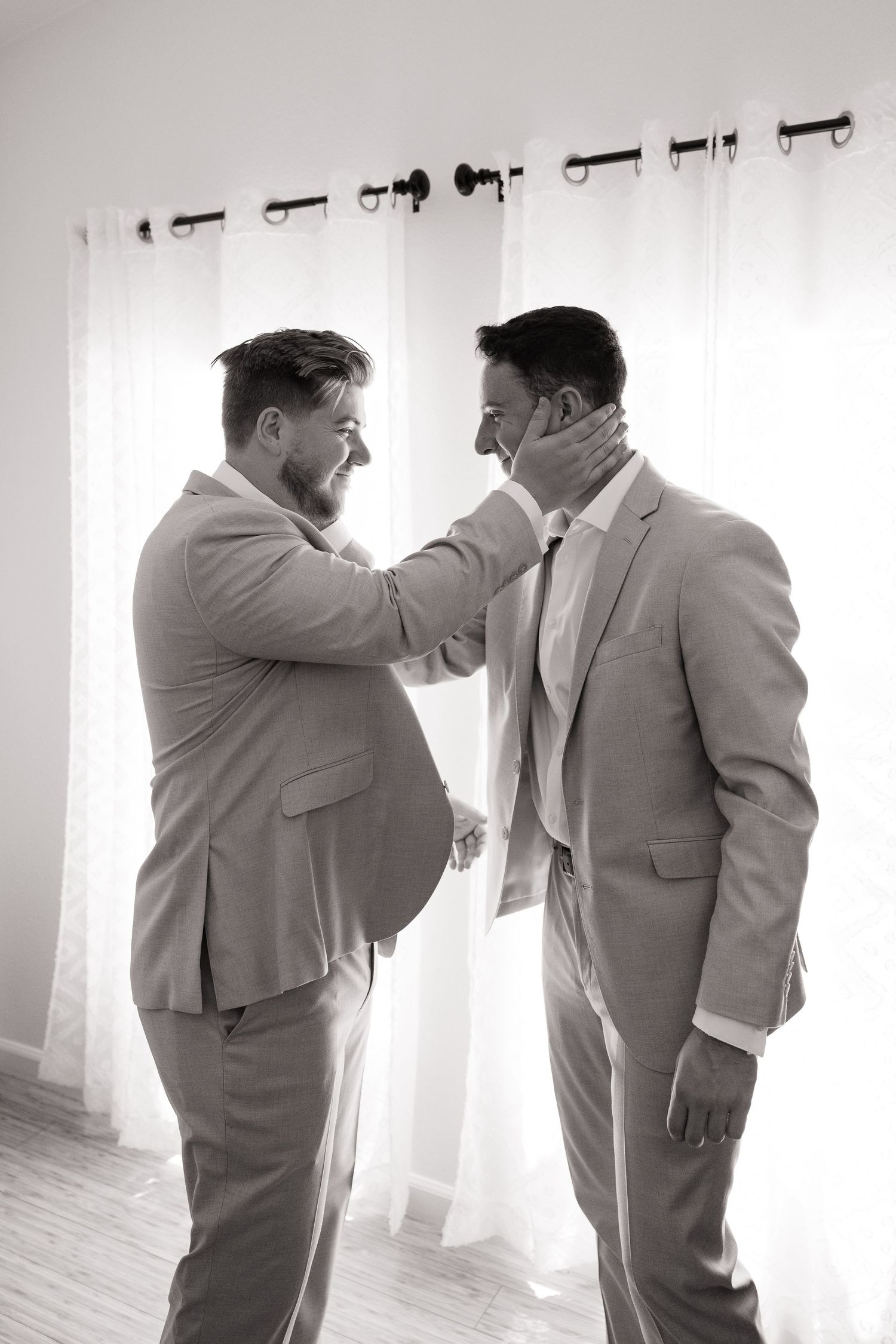 Black and white photo of two groomsmen helping each other with neckties.