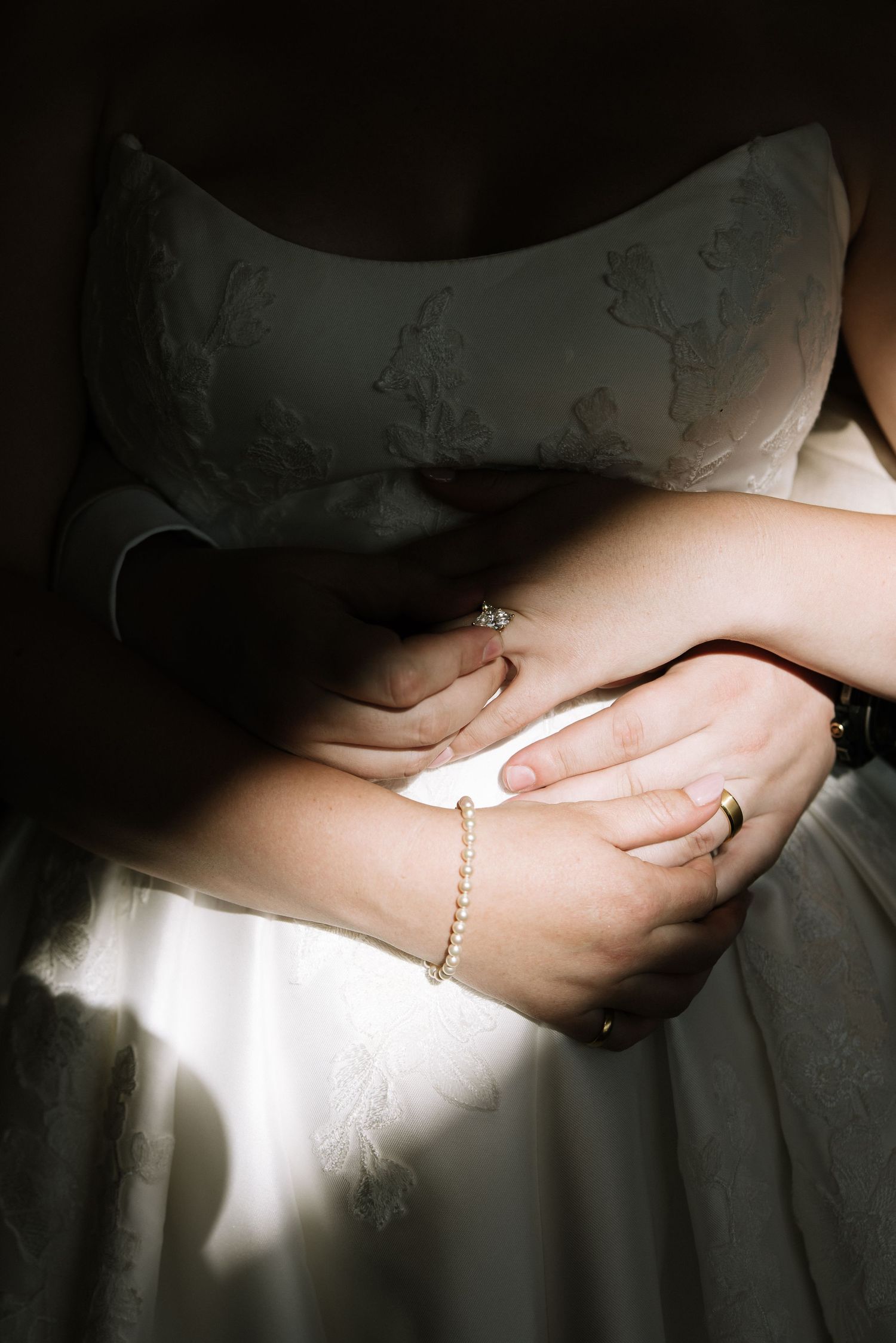 Close-up of bride and grooms hands intertwined showing wedding rings and delicate pearl bracelet.