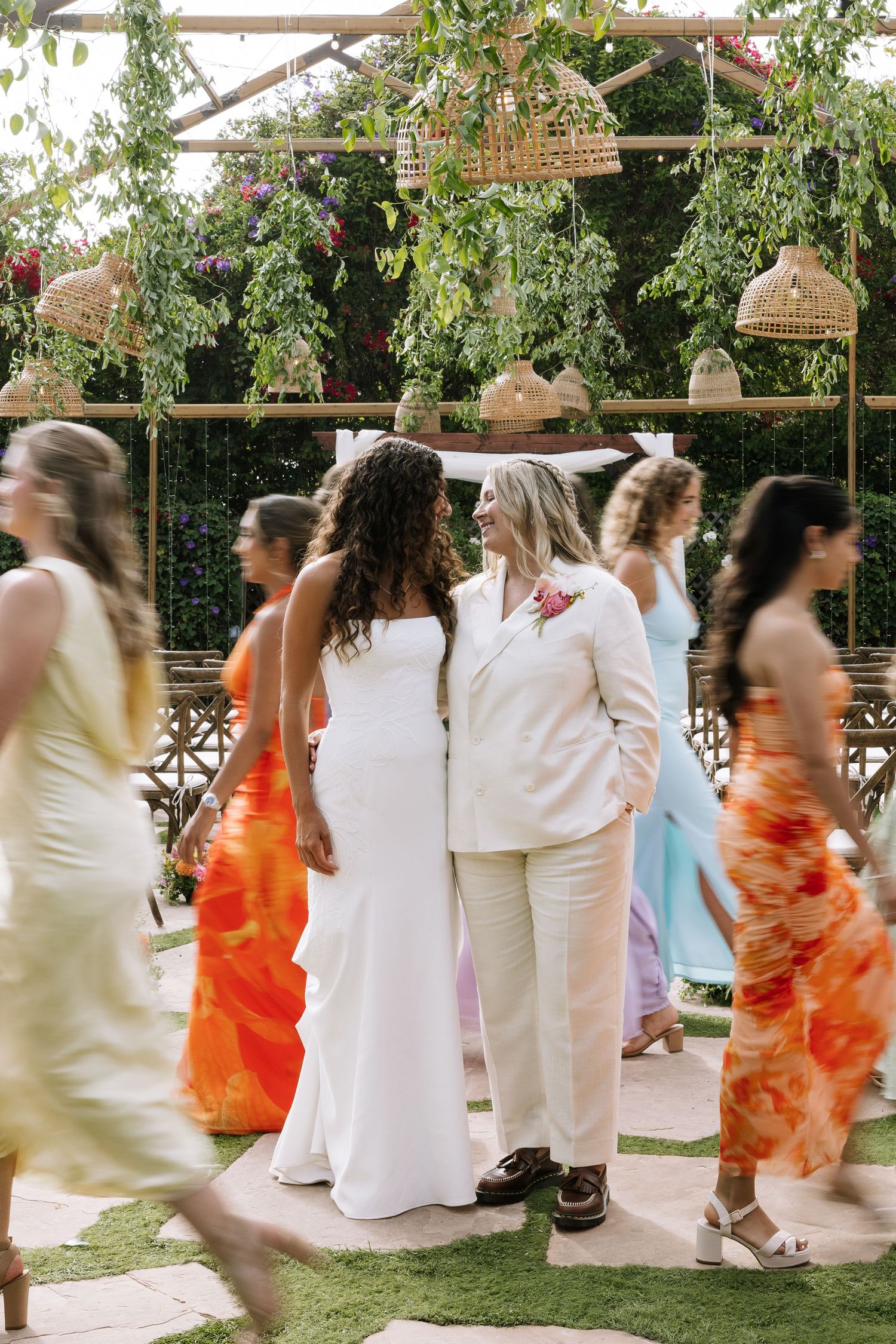 Two brides share a joyful moment at an outdoor ceremony with a floral wooden arch.
