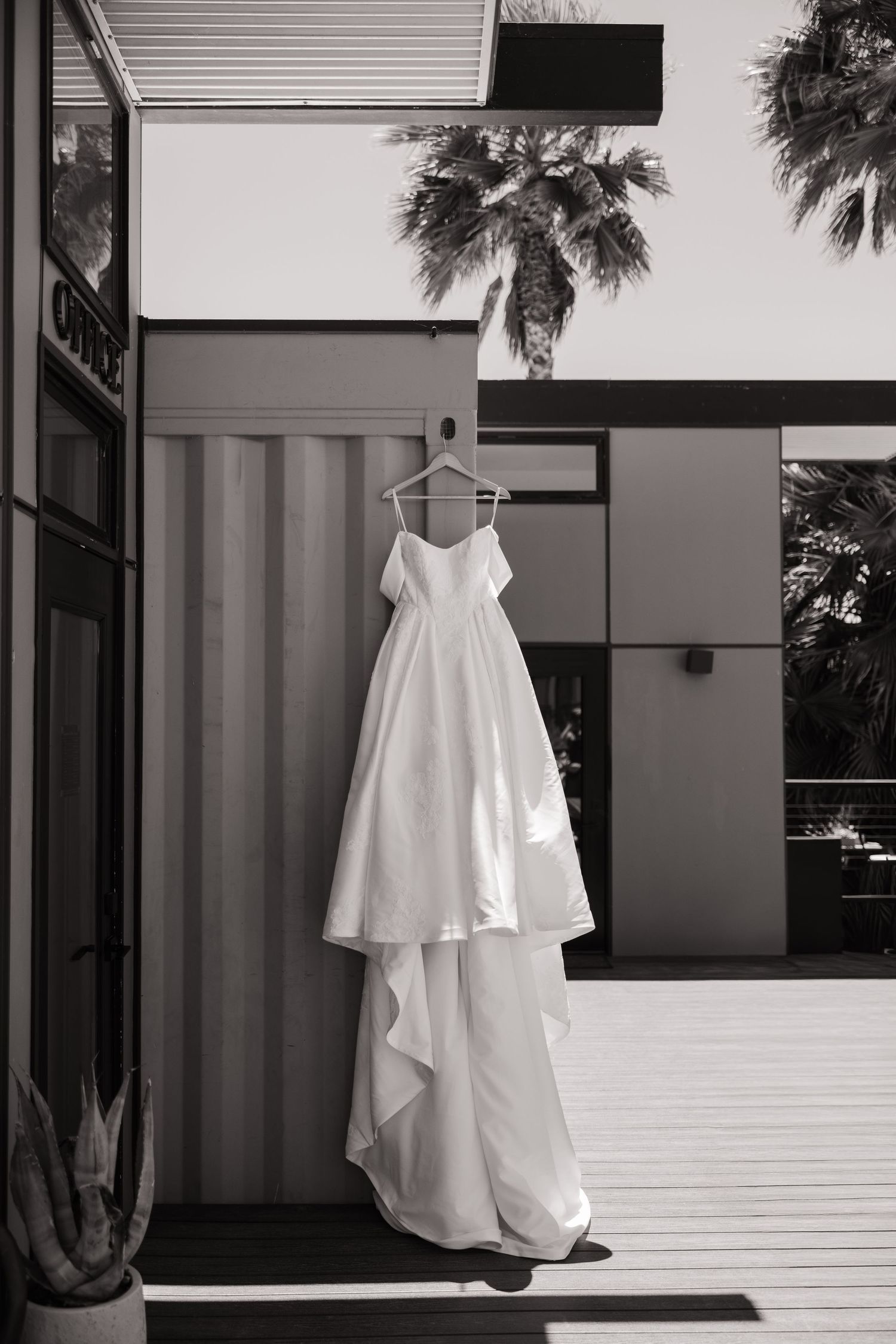 Classic white spaghetti strap wedding dress with cascading train displayed on hanger at modern venue.