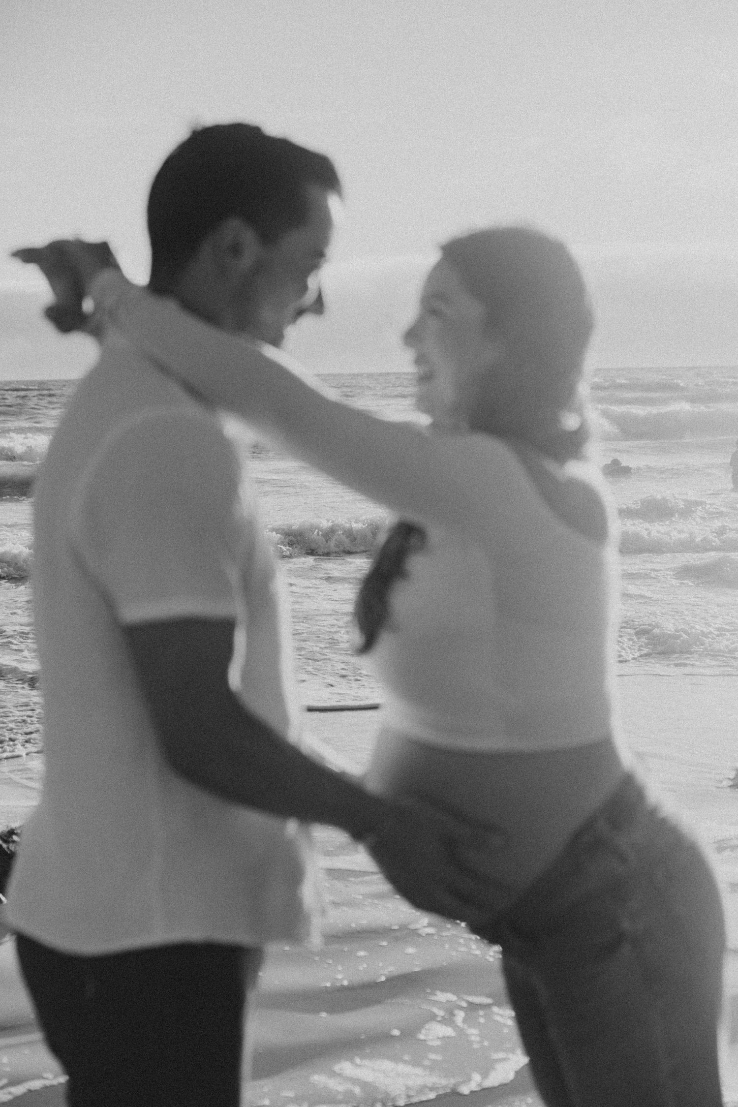 Black and white photo of a couple dancing romantically on a beach with ocean waves in the background.