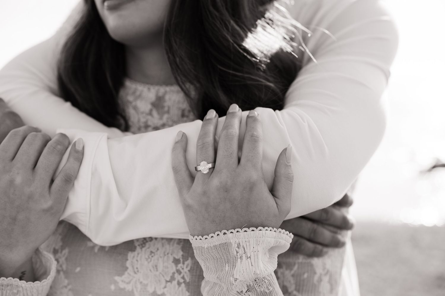 Black and white close-up of a couple embracing, showcasing a stunning diamond engagement ring.