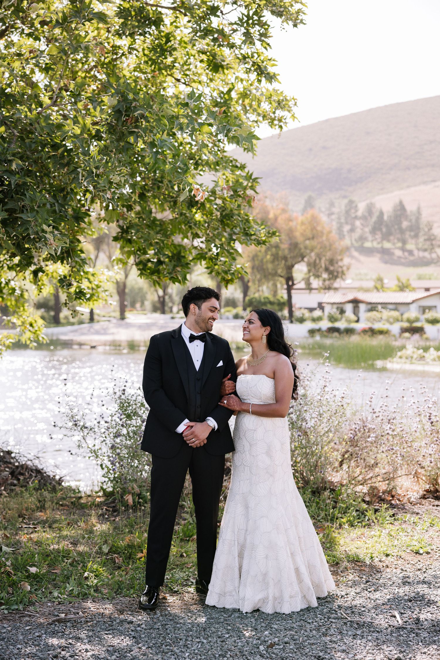 Bride and groom share a romantic moment by a scenic lake surrounded by lush greenery and rolling hills.