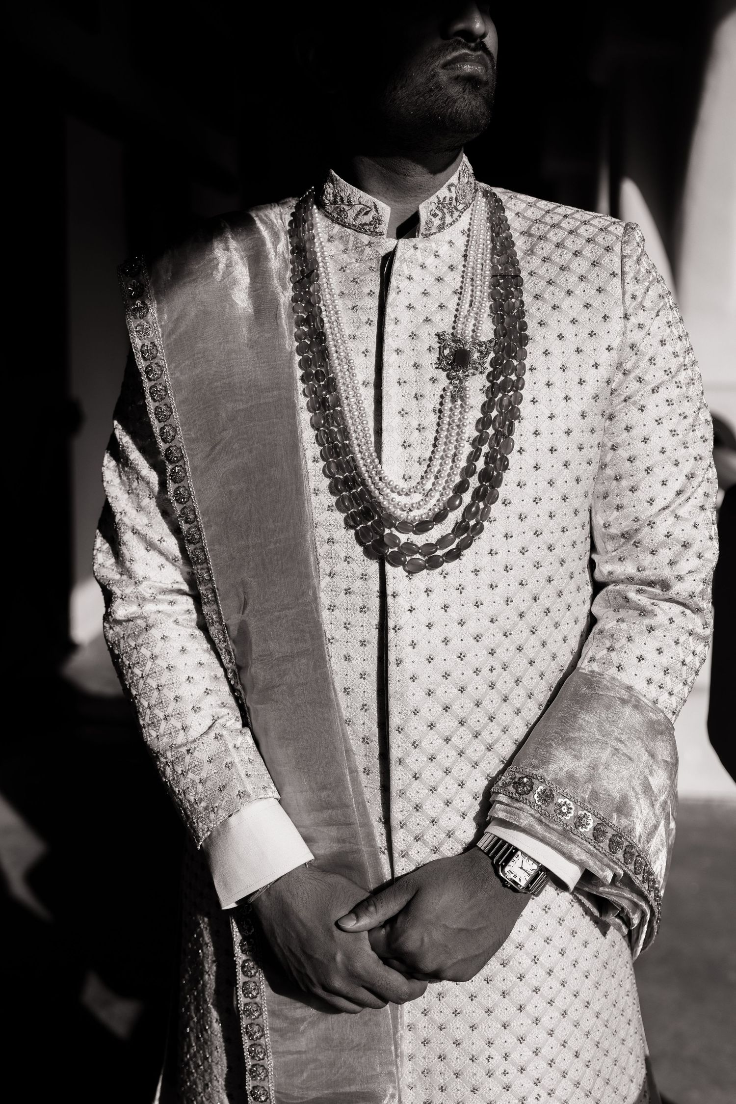 Groom wearing traditional embroidered sherwani and layered necklaces in black and white photo.