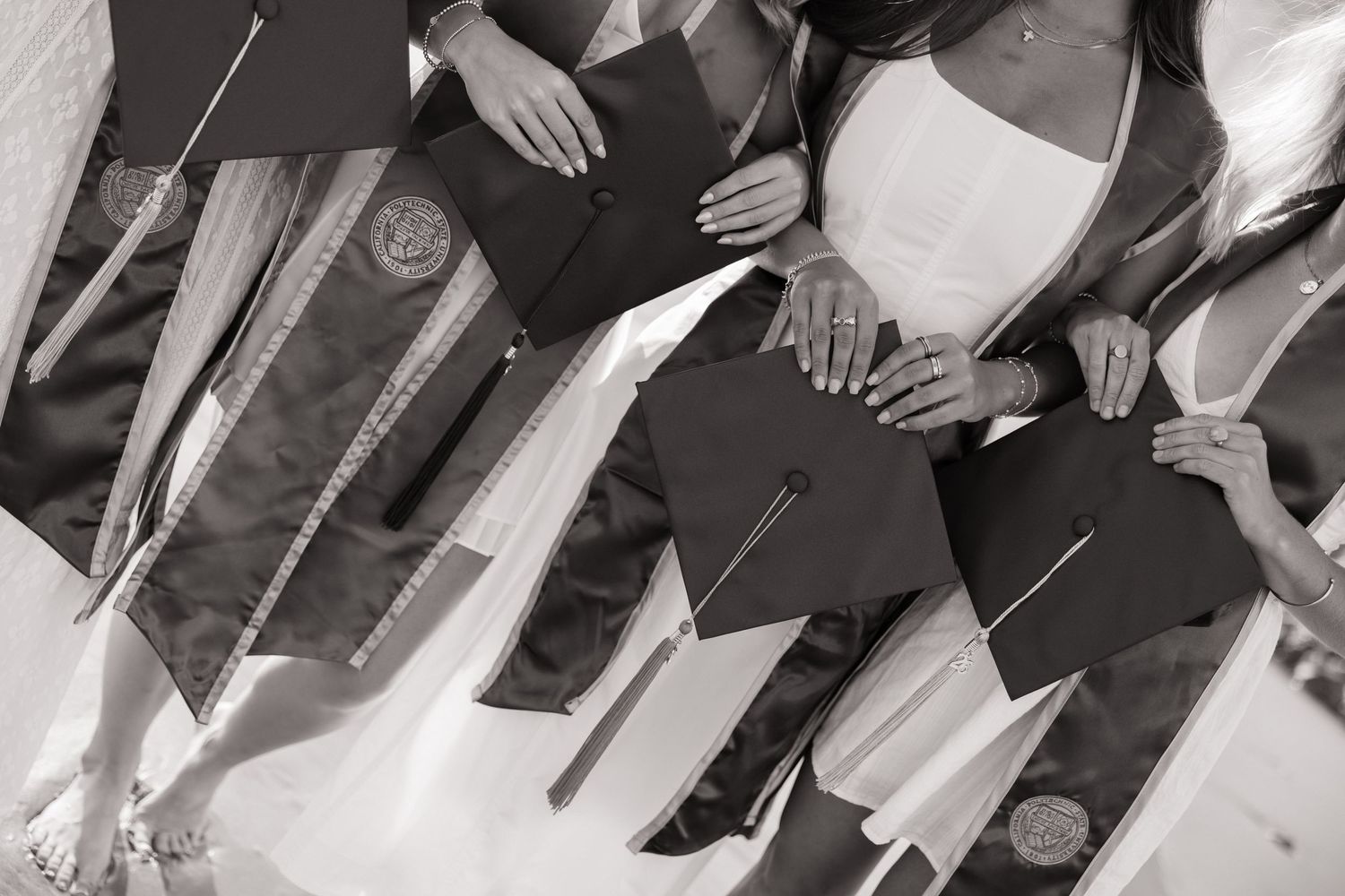 Close-up black and white photo of four graduates holding diplomas with green graduation stoles.