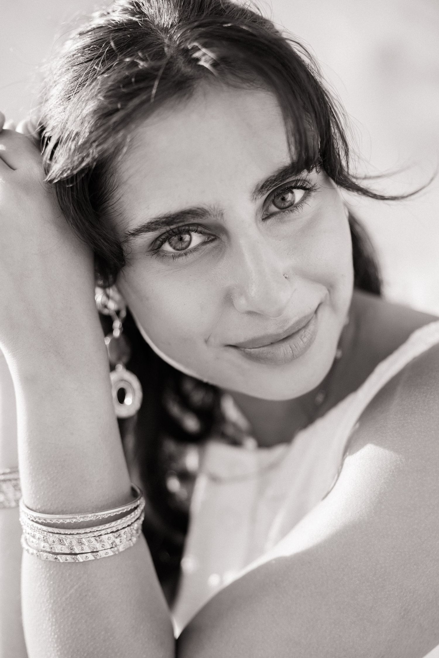 Close-up black and white portrait of a young woman with dark hair wearing earrings and bracelets.