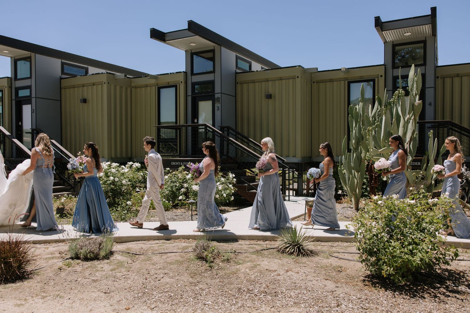 Bridesmaids in blue dresses walking with bride outside modern venue.
