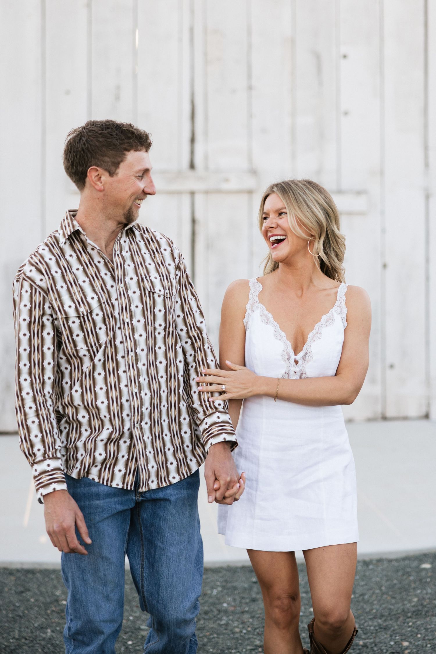 Happy couple holding hands and laughing together in front of a white barn door.