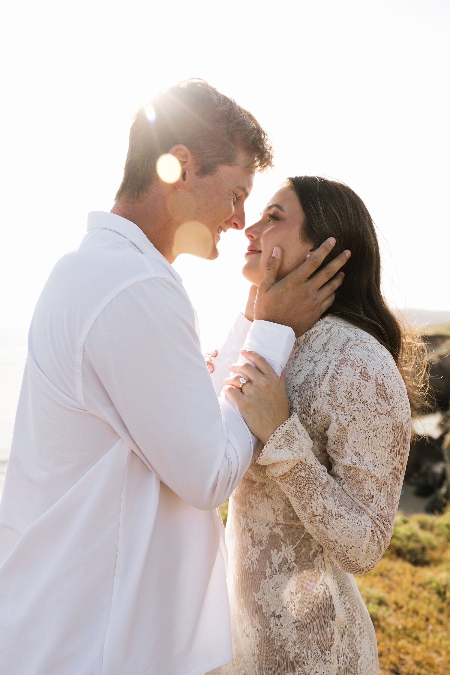 Couple sharing intimate moment in golden sunlight, woman in lace dress tenderly touching mans face.