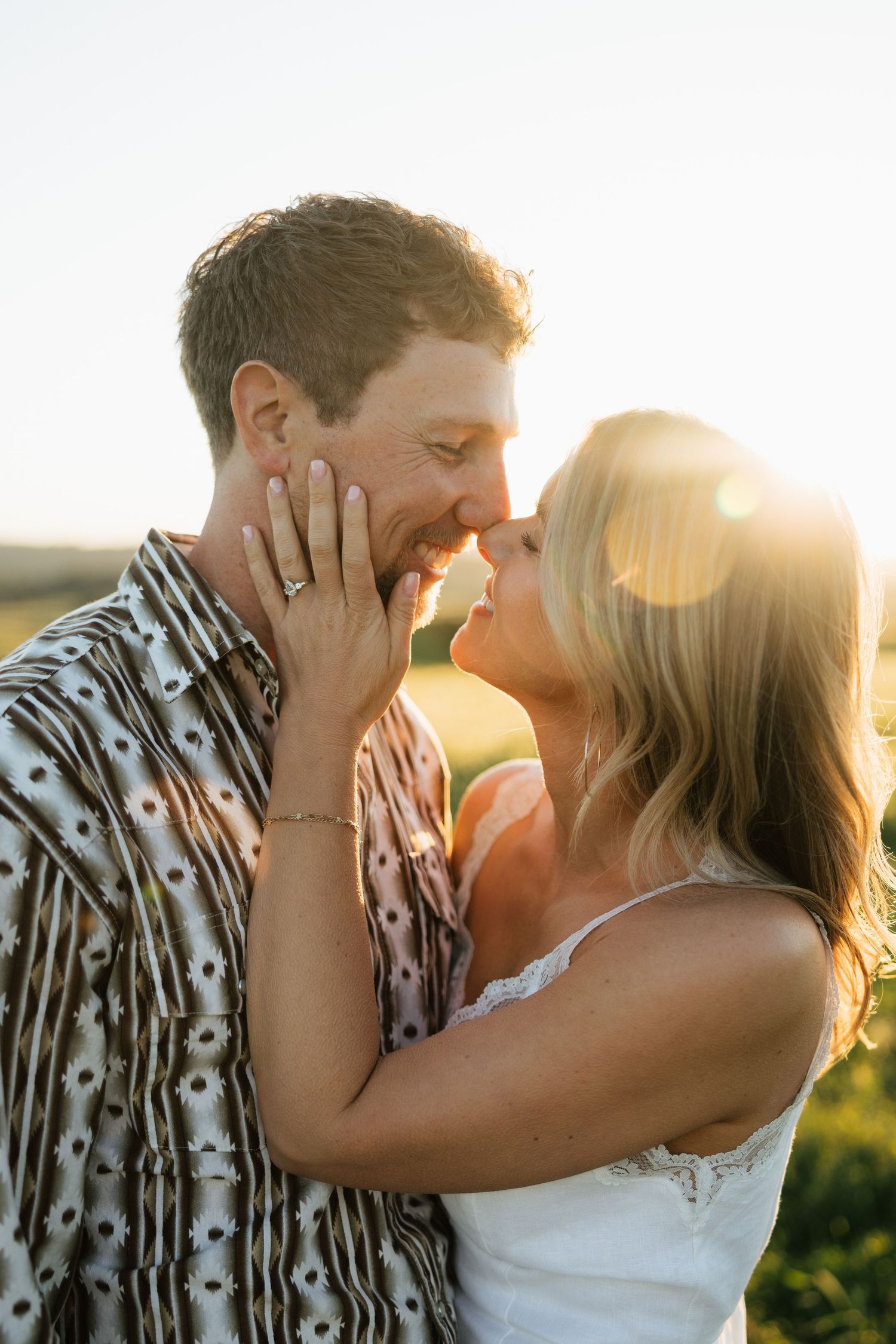 Couple nearly kissing at golden sunset in open field with warm backlit glow.