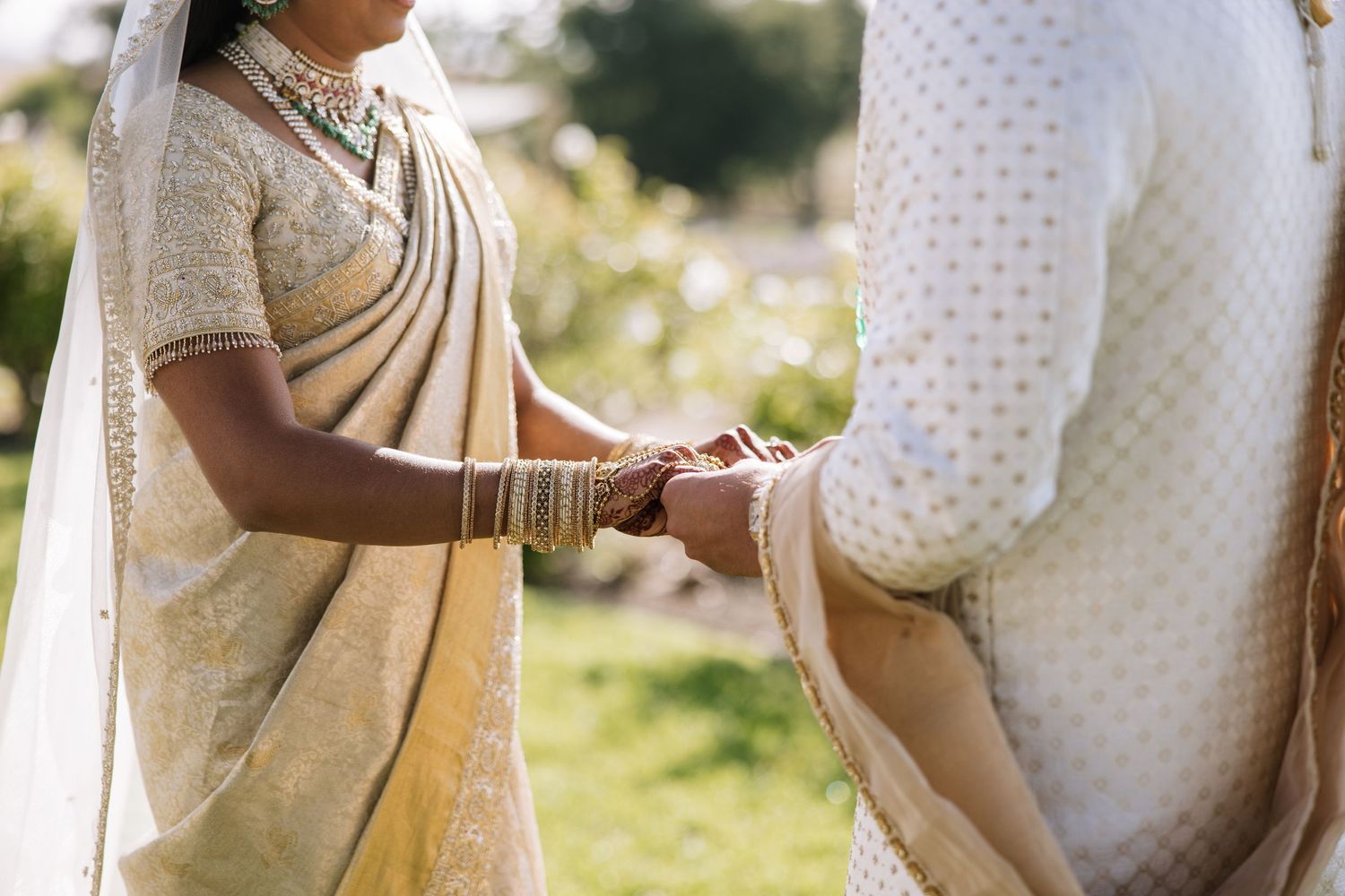 An Indian bride in a gold saree exchanges rings with her groom during an outdoor wedding ceremony.