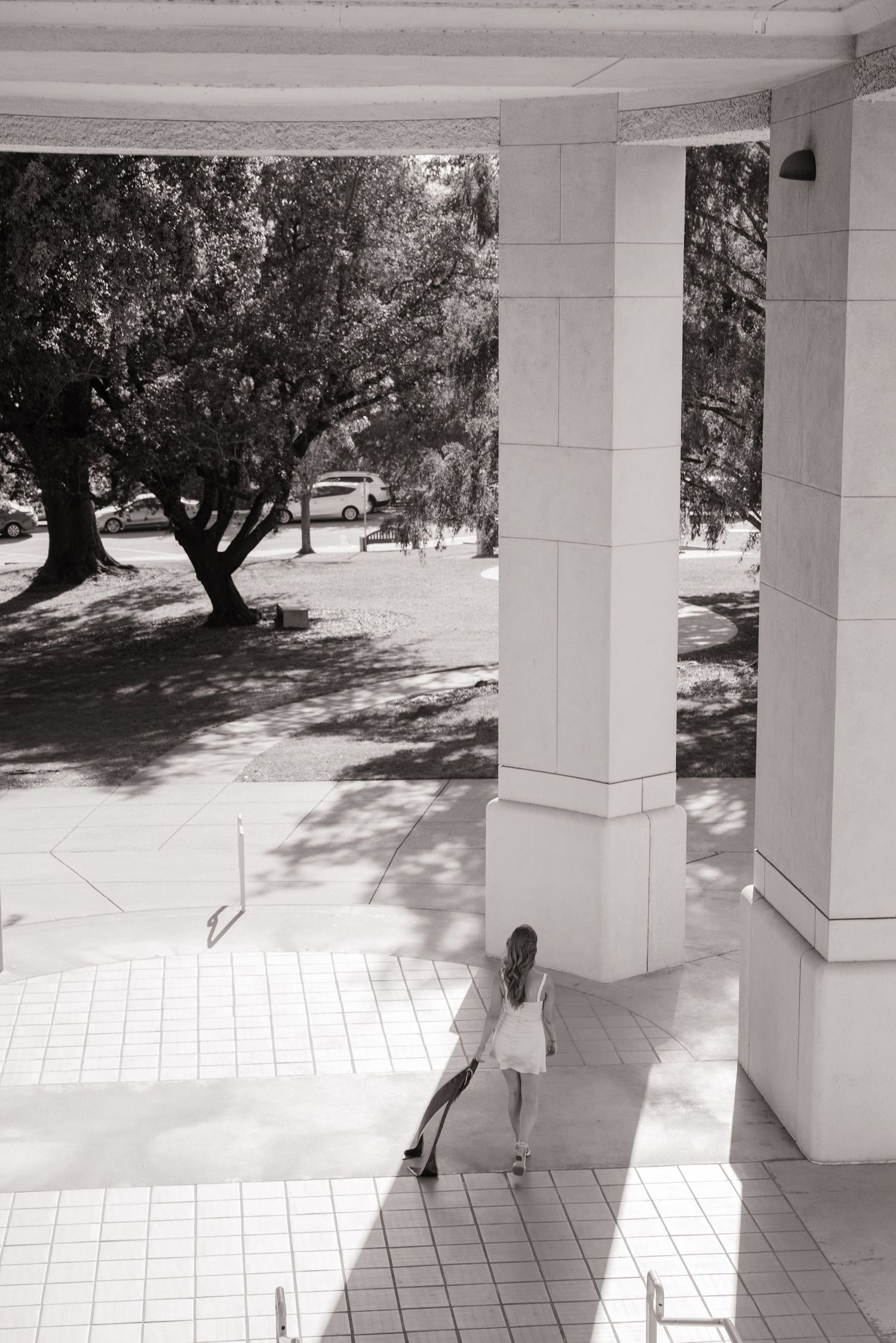 Black and white aerial view of woman in white dress walking between large columns.