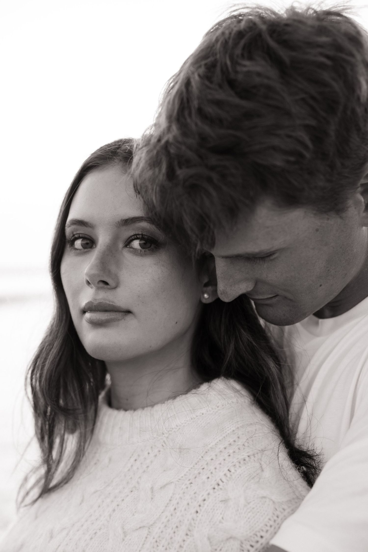 Intimate black and white portrait of engaged couple on beach with tender expressions.