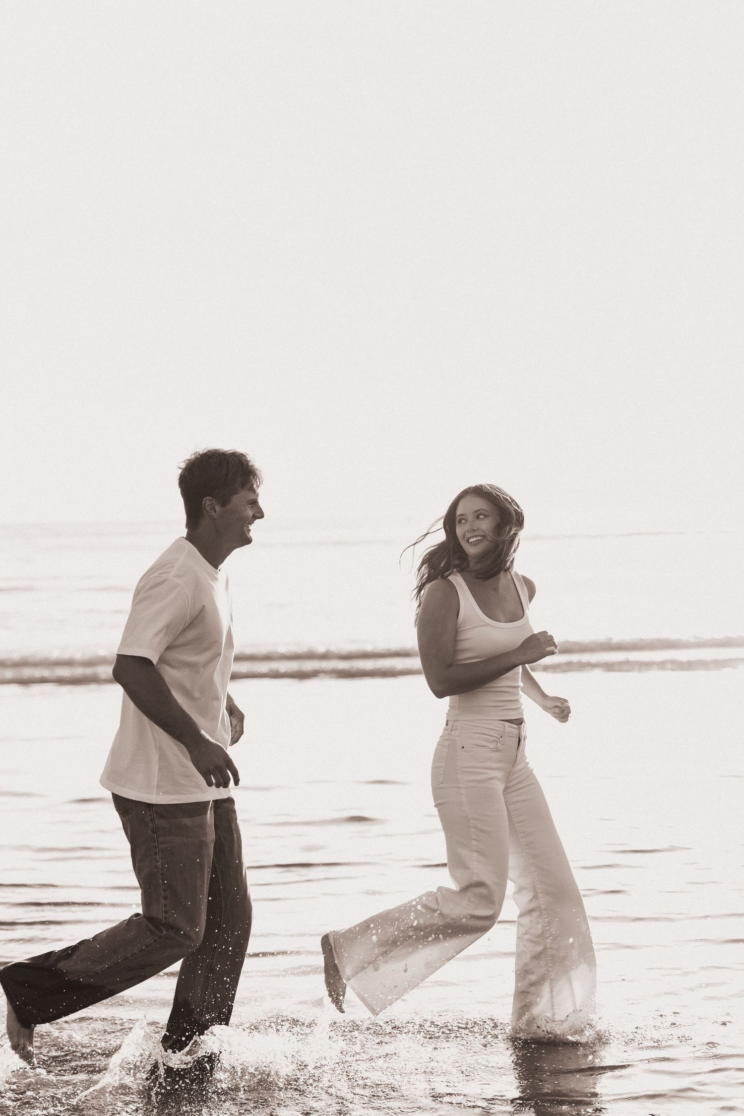 Joyful couple running and splashing through ocean waves on beach in sepia tone.