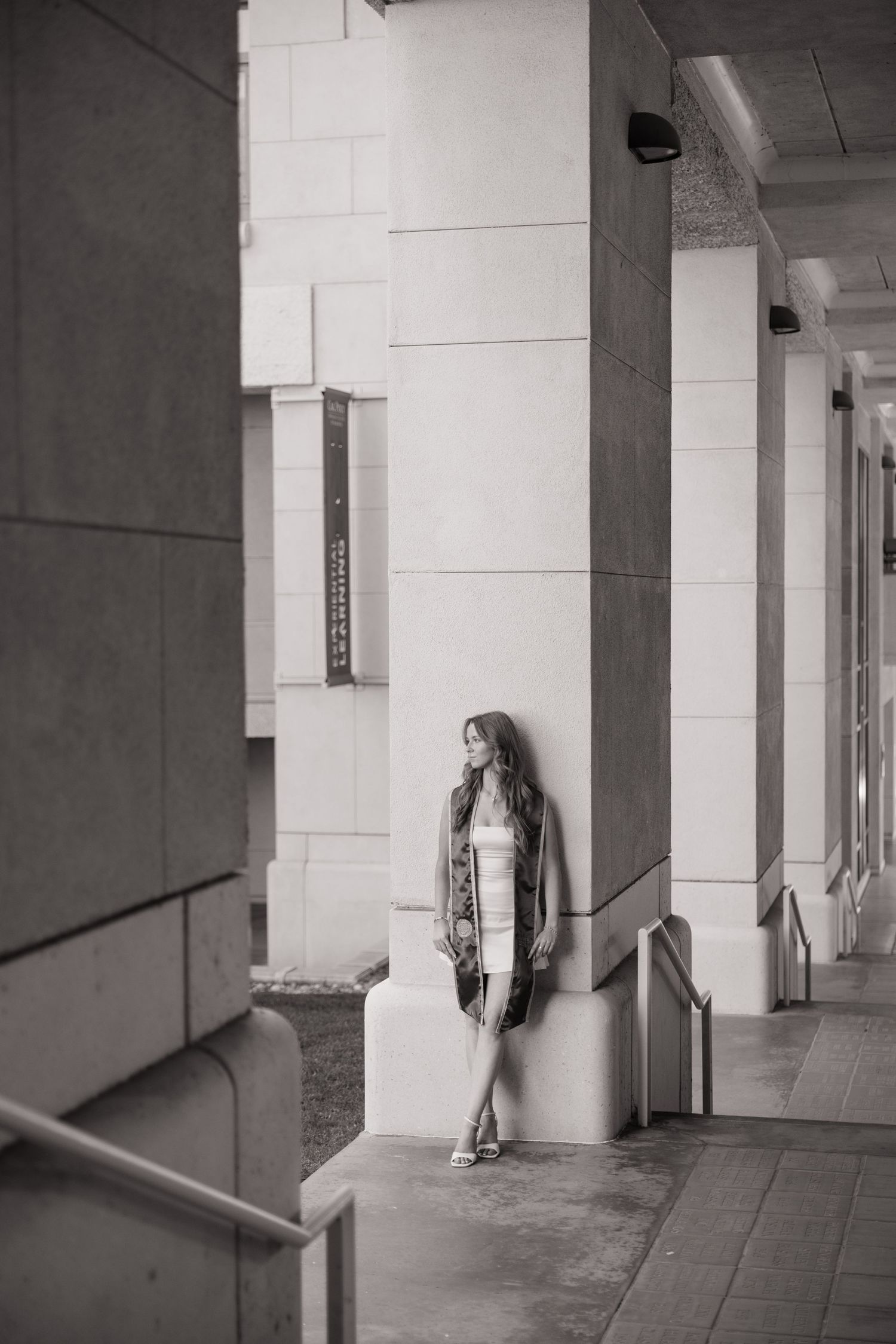 Black and white photo of woman in white dress leaning against column in arcade.