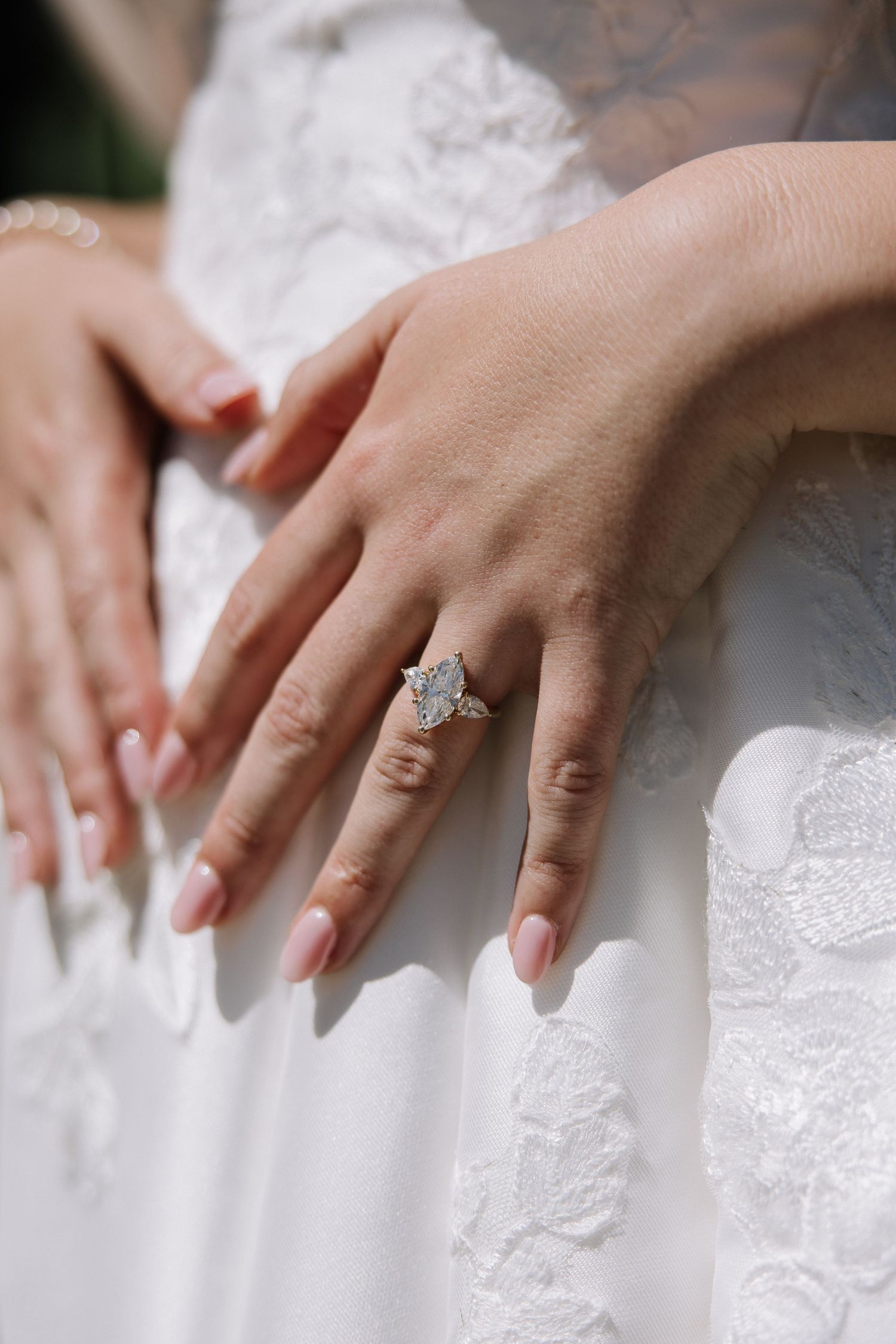 Close-up of bride's hand showing large diamond engagement ring on lace gown.