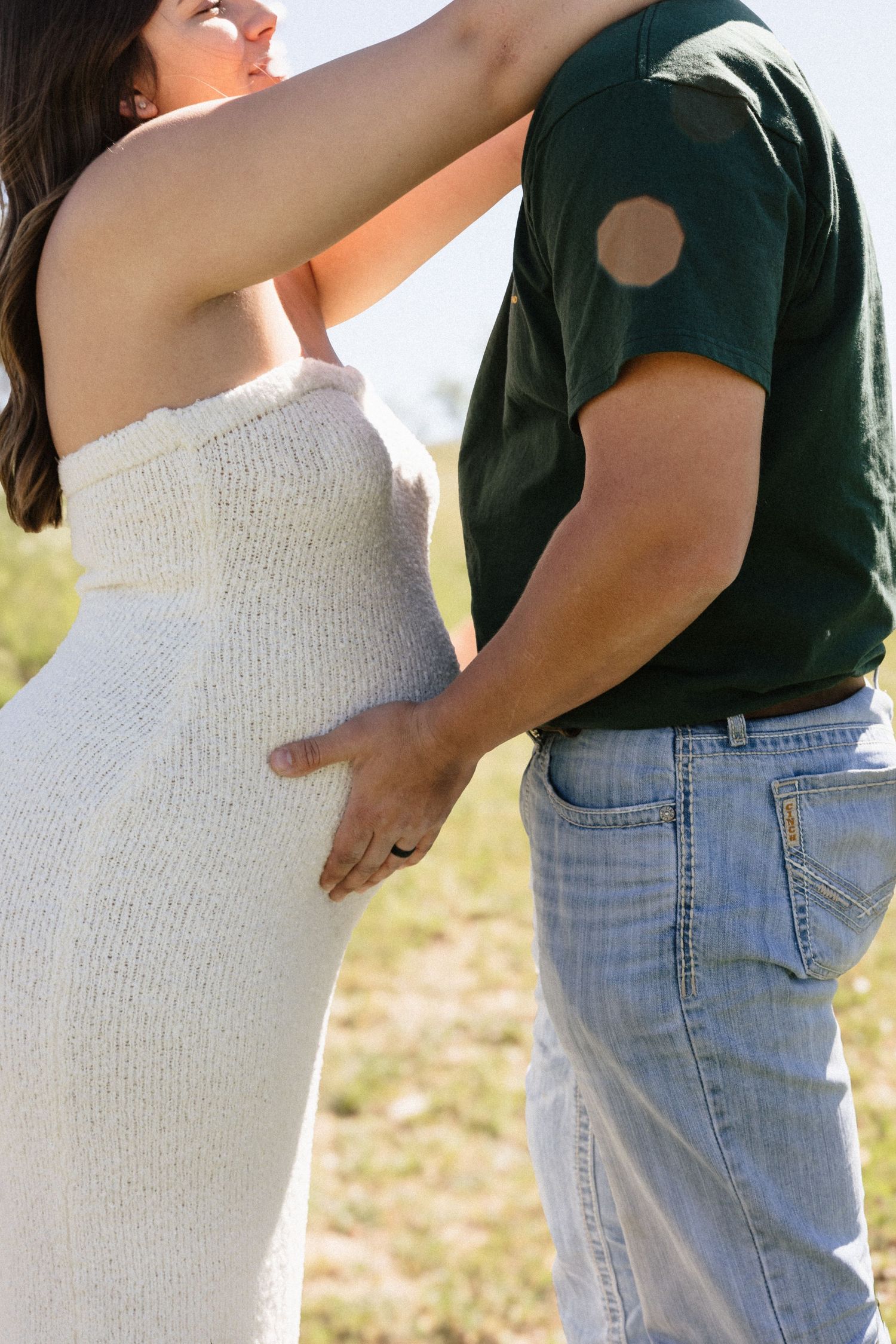 Couple sharing tender moment outdoors, man placing hand on pregnant womans baby bump.