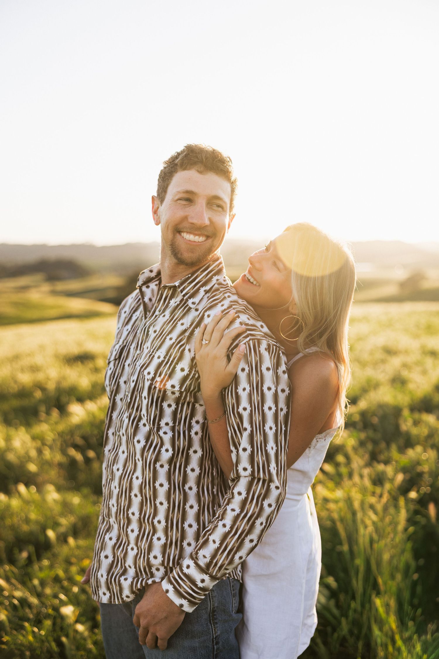 Joyful couple embracing in a sunlit green field at golden hour sunset.