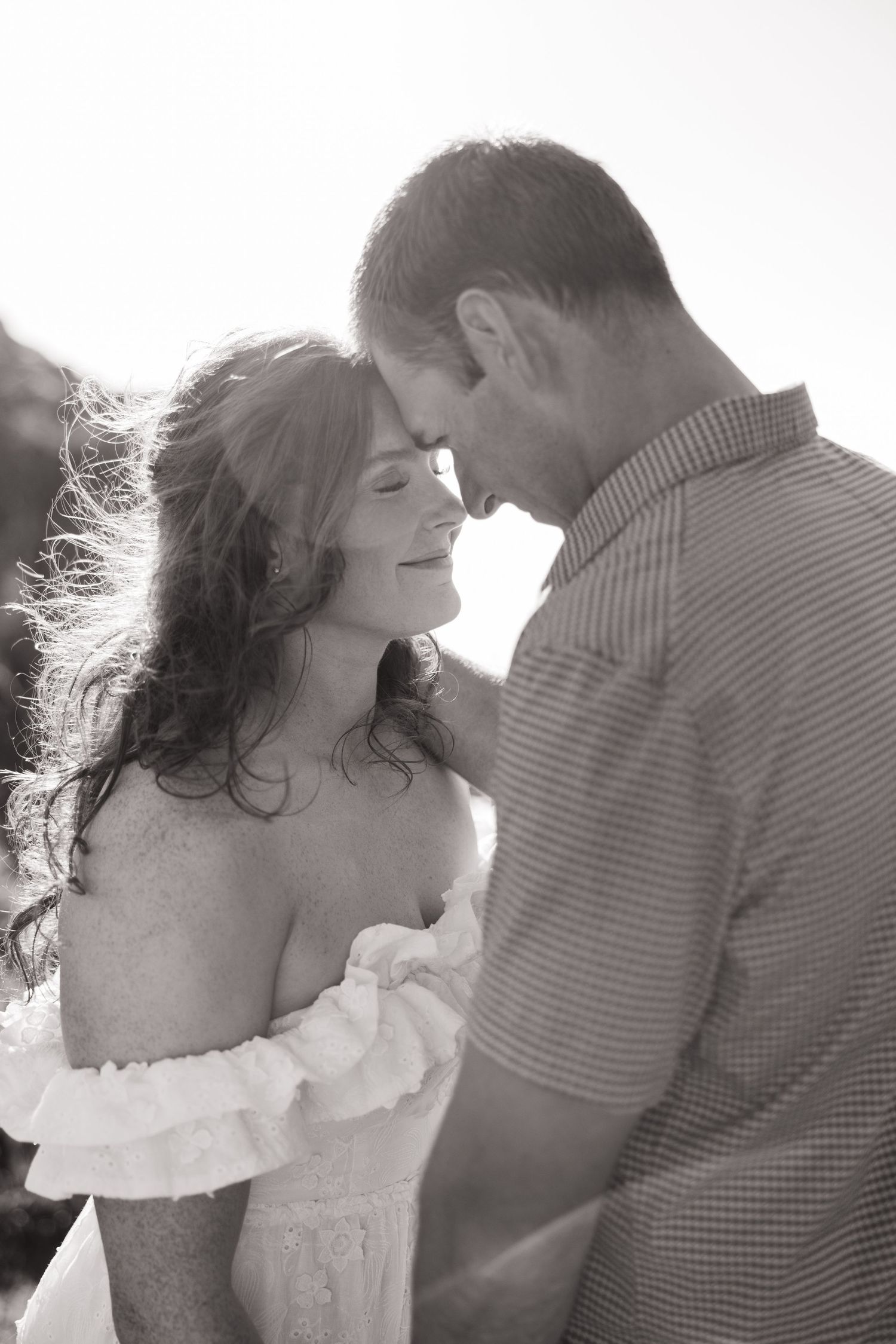 Intimate black and white portrait of couple touching foreheads in romantic outdoor setting.