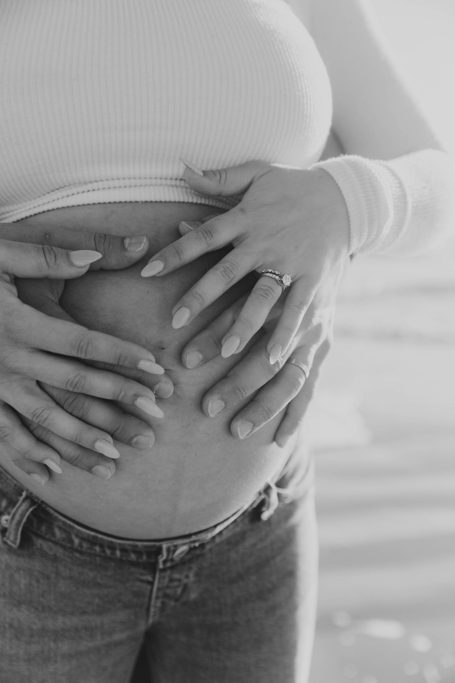 Close-up black and white photo of a pregnant woman's baby bump with both partners' hands cradling it.