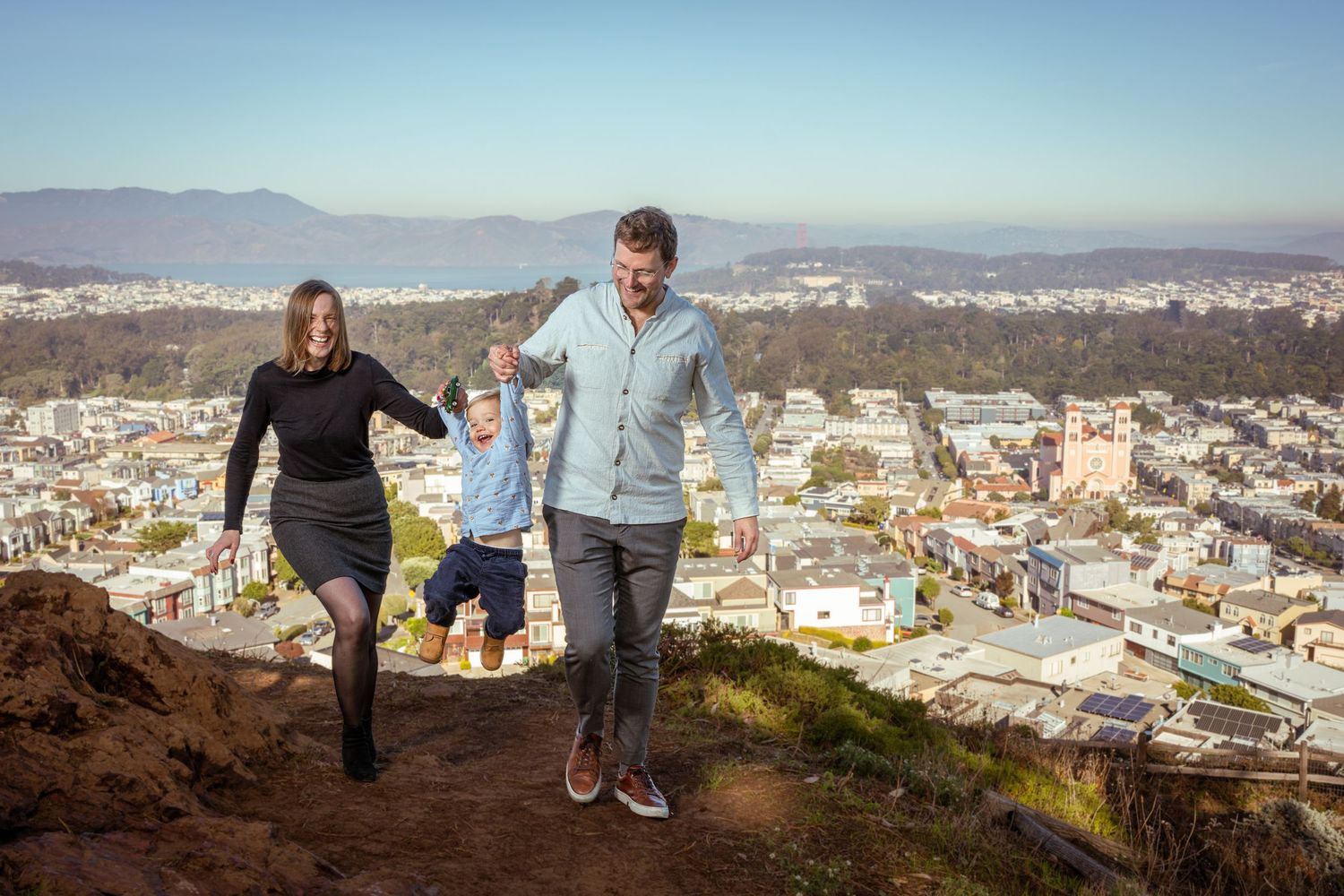 Couple holding hands while hiking up steep trail with city view below.
